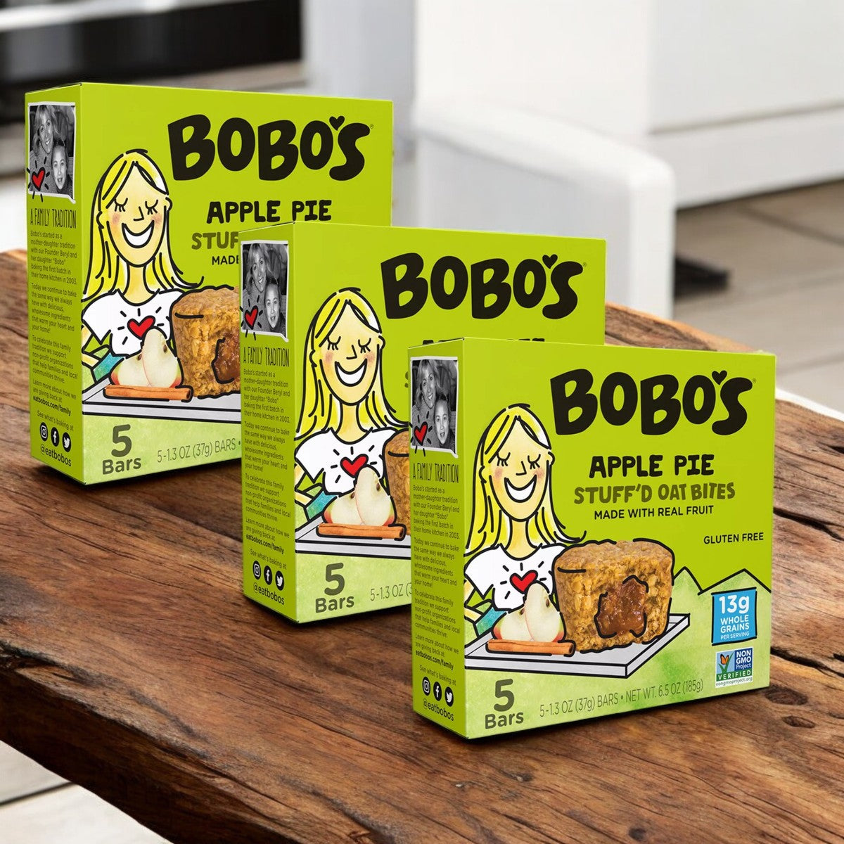 Three 20-count boxes of Bobo's Apple Pie Filled Bites sit on a wooden table. These convenient snacks, made by Bobo's with wholesome ingredients, let you enjoy the comforting taste of apple pie anywhere.