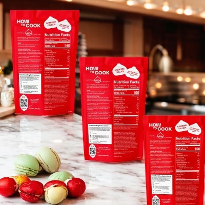 Three packages of Mila 3 Pack Soup Dumpling Combo, with nutrition facts displayed, stand on a kitchen countertop, suggesting the authentic flavors of Mila soup dumplings. In the foreground, a small pile of colorful macarons adds a whimsical touch to this culinary scene.