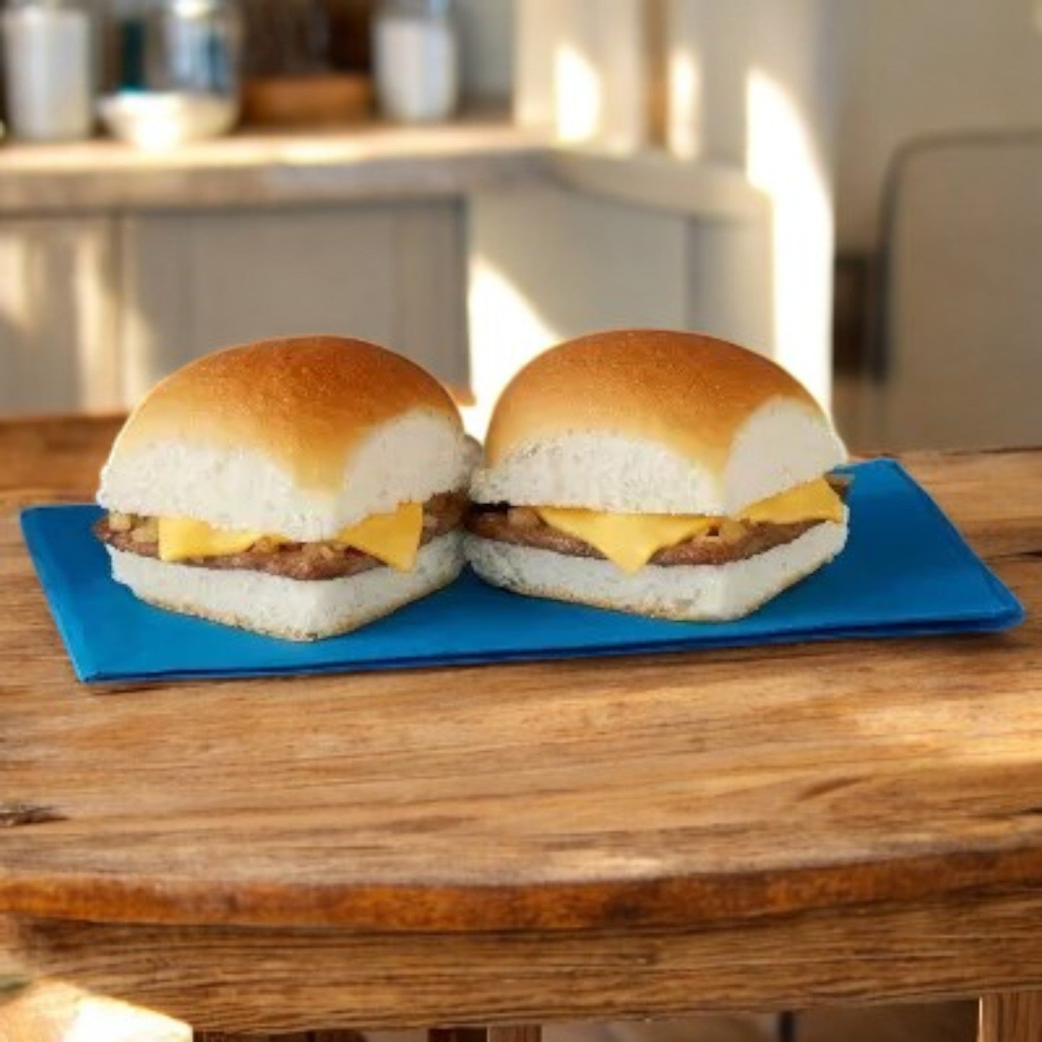 Two sliders from the White Castle 3 Pack Combo sit enticingly on a blue rectangular plate, reminiscent of classic cheeseburgers, placed invitingly on a wooden table.