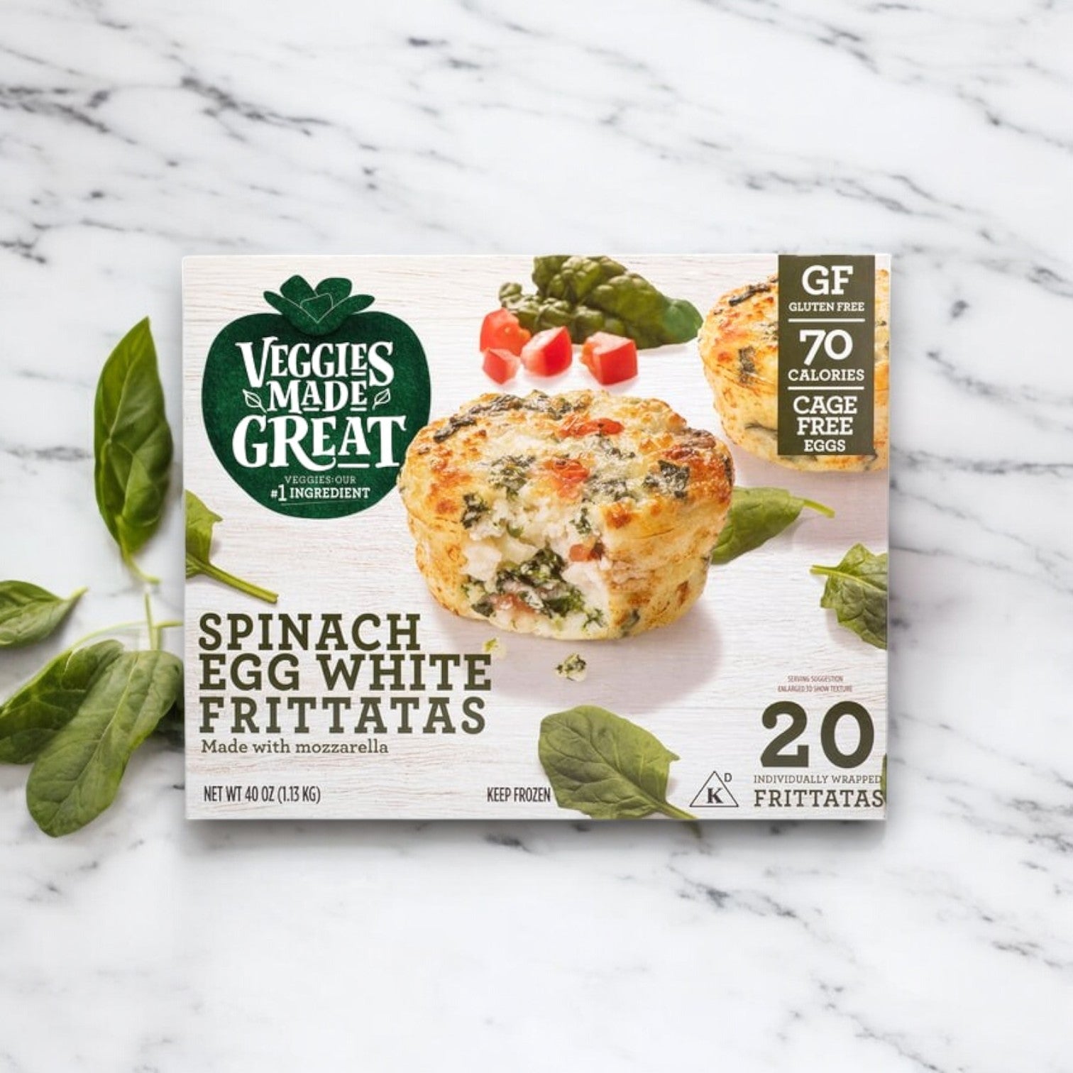 A Veggies Made Great Garden Lites Vegetarian Spinach & Egg White Frittata box on marble, surrounded by spinach. These gluten-free, mozzarella-infused bites are a protein-rich, low-calorie breakfast option with each frittata at just 70 calories.