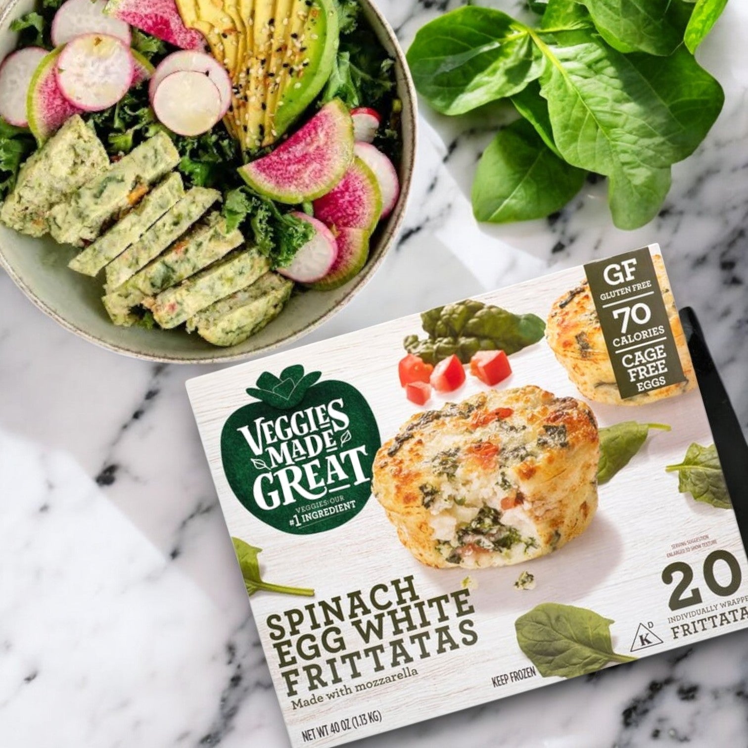A box of Veggies Made Great Garden Lites Vegetarian Spinach & Egg White Frittatas (20-count) sits by a salad with radishes, avocado, and spinach on a black-and-white surface. Ideal for a protein-rich, low-calorie breakfast to kickstart your day.