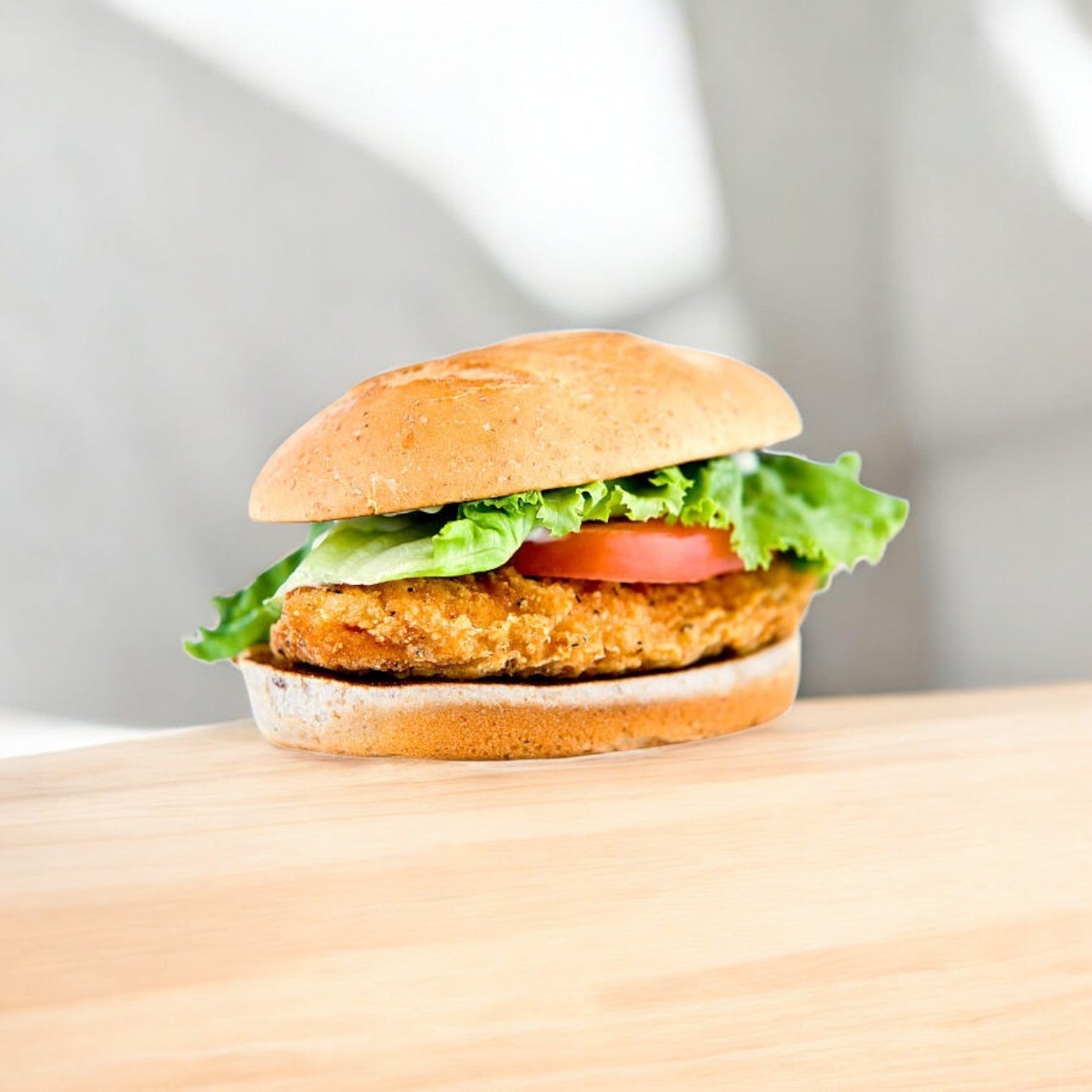 A sandwich with Garden Valley Breaded Halal Chicken Breast Patties, fresh lettuce, and tomato sits on a rustic wooden surface.