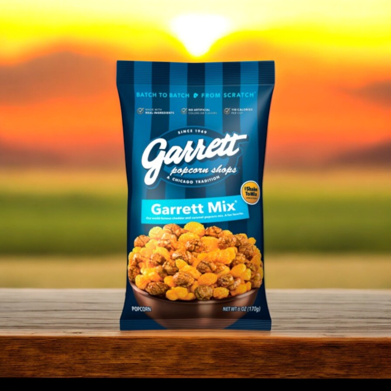 A 6 oz. bag of Garrett Popcorn's Garrett Mix, featuring a delicious blend of CheeseCorn and caramel, rests on a wooden surface with a blurred sunset backdrop.