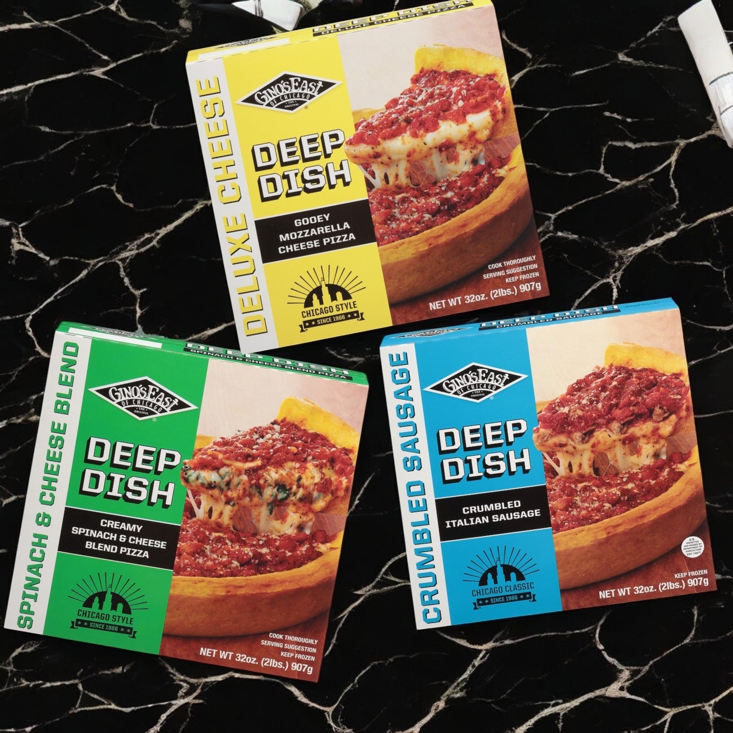 Three boxes from the Gino’s East Pizza Bundle, featuring their signature golden crust, are placed on a marble surface. The flavors include Deluxe Cheese, Spinach & Cheese Blend, and Crumbled Sausage by Gino's East Pizza.