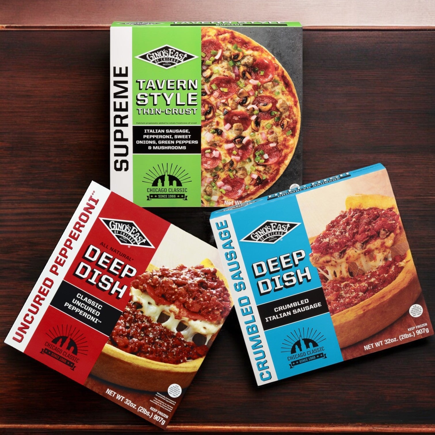 Three Gino's East frozen pizzas sit on the wooden surface: a Supreme Tavern Style, a Deep Dish Uncured Pepperoni Pizza, and a Deep Dish Crumbled Sausage. This Gino's East Variety Pack offers detailed descriptions and brand logos, perfect for any pizza lover.