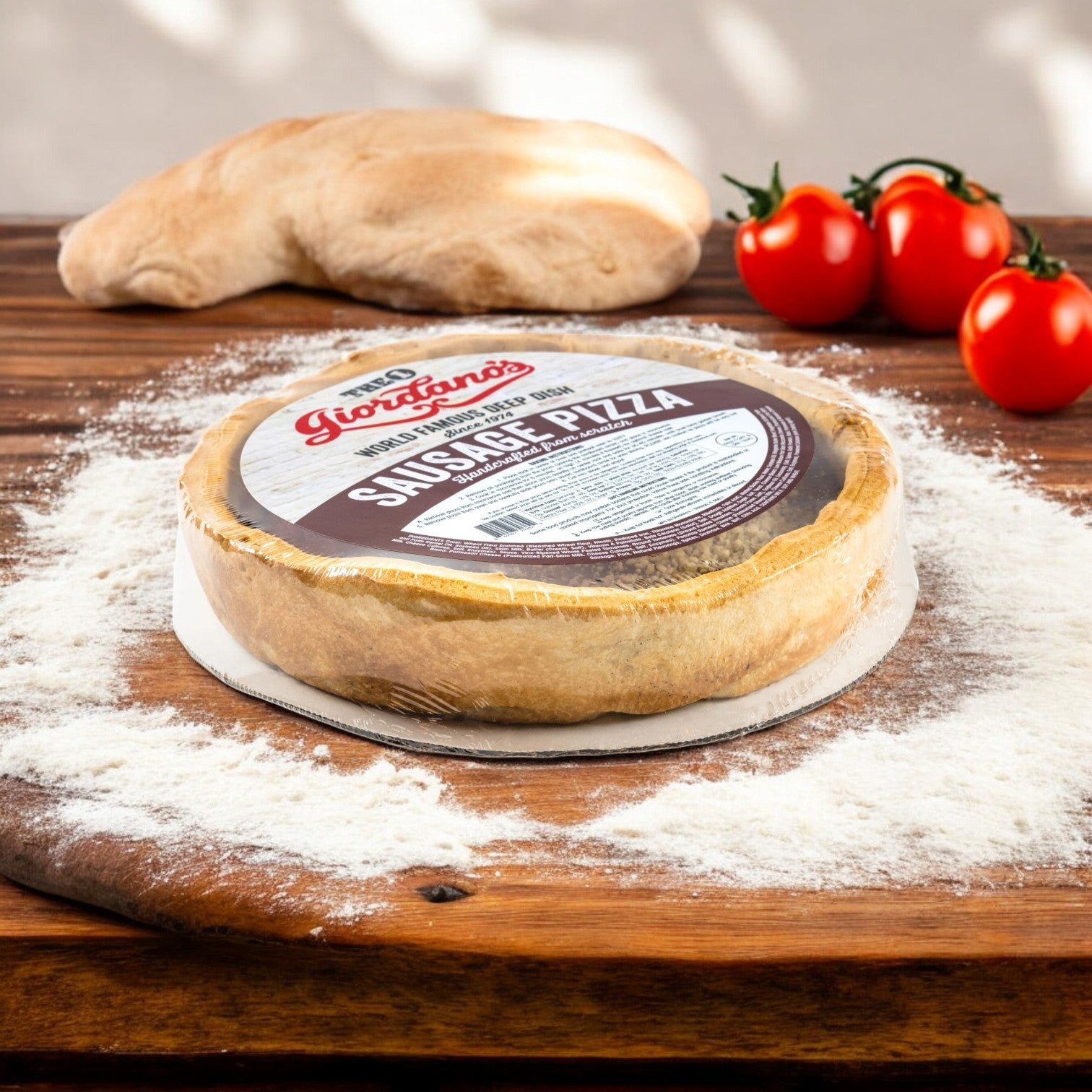 A Giordano's Frozen Deep Dish Stuffed Sausage Pizza rests on a flour-dusted wooden board beside fresh dough and three ripe tomatoes, evoking a Chicago deep dish masterpiece.