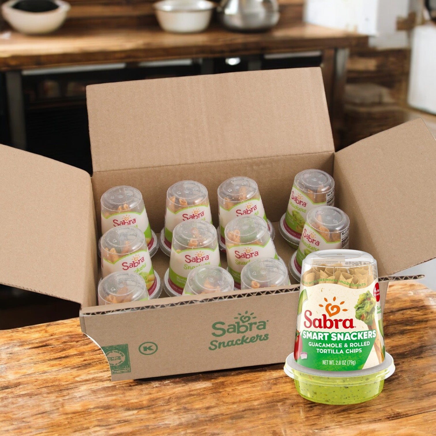 A case of Sabra Guacamole with Rolled Tortilla Chips, featuring creamy Hass avocado guacamole and crispy chips, neatly arranged on a wooden table; 2.8 oz packs, 12 per case.
