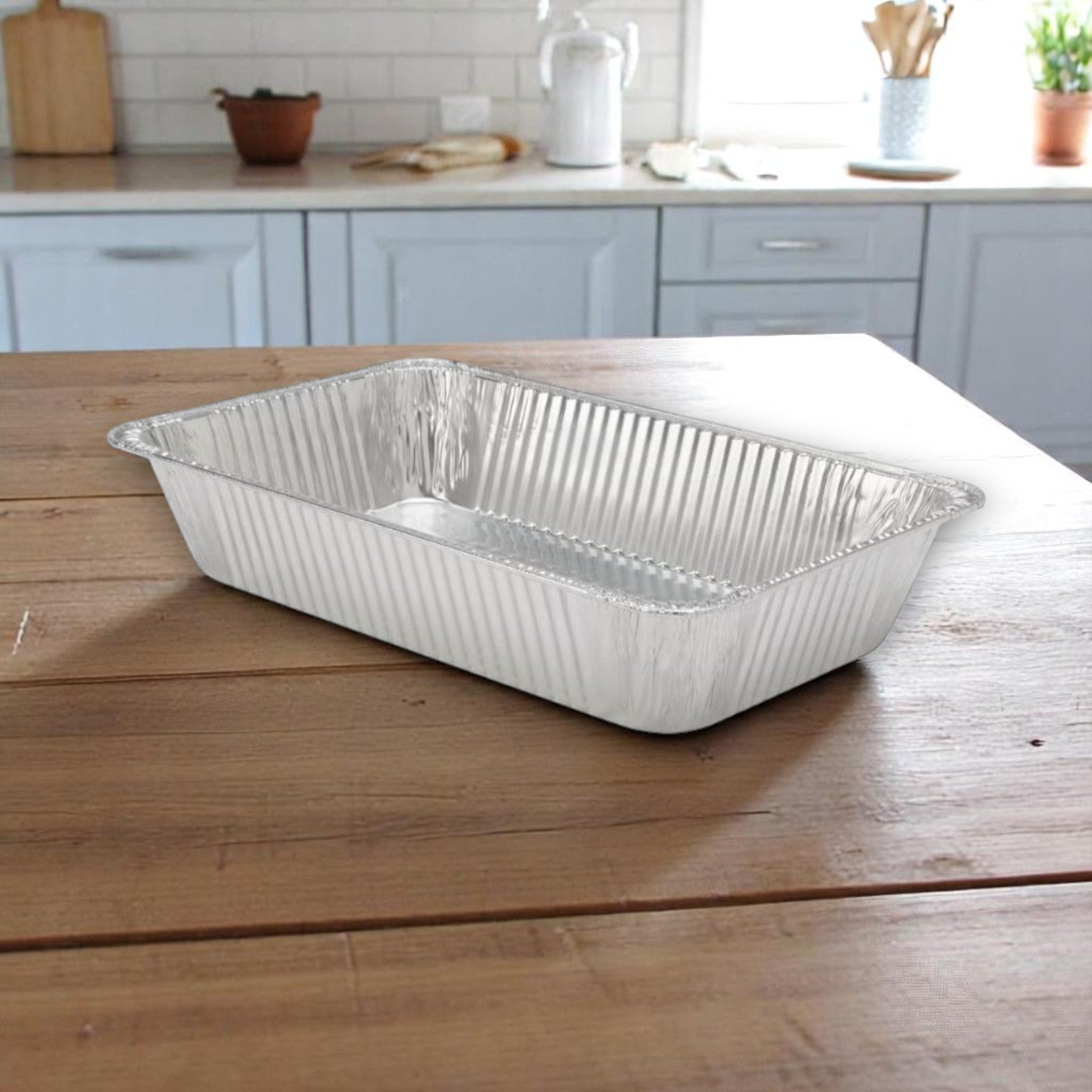 A Handi-Foil of America HFA Deep Full-Size Steam Table Pan from the 10-pack heavy-duty aluminum set for catering and events sits on a wooden kitchen table, with a modern kitchen in the background.