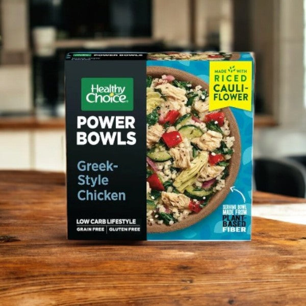 A Healthy Choice Power Bowls box with Greek-Style Chicken is on a wooden table, featuring riced cauliflower for a grain-free and gluten-free meal.