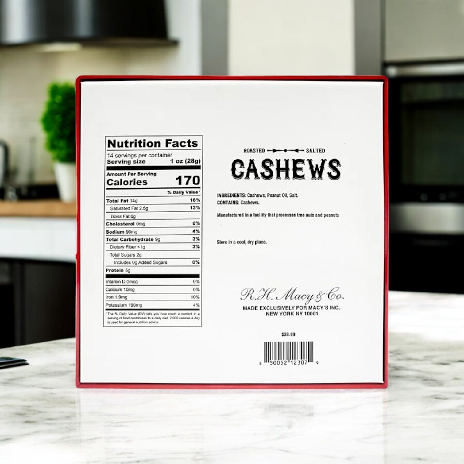 Displayed on the kitchen counter, Macy’s Roasted Salted Jumbo Cashews Gift Box (14 oz) from R.H. Macys & Co. showcases nutrition facts and ingredients. At $19.99, it's a premium holiday gift box addition featuring jumbo cashews and festive packaging.