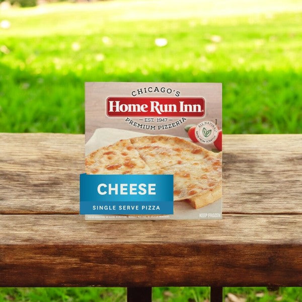 A box of "Home Run Inn Mini Personal Pizza, Classic Frozen Cheese Pizza, 7.5 oz. - 1 Count" sits enticingly on a wooden bench against a grassy backdrop, inviting pizza enthusiasts to enjoy its rich mozzarella cheese.