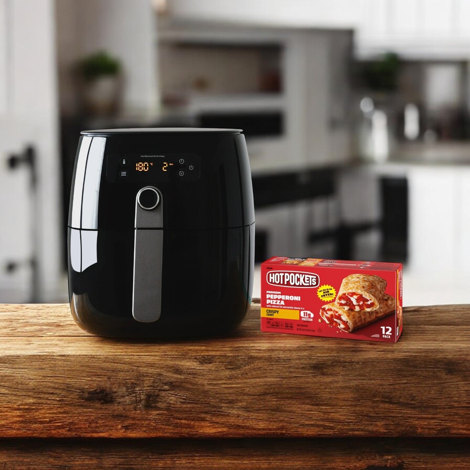 A black air fryer sits elegantly on the wooden counter, enhancing the kitchen setting, with a pack of Hot Pockets Frozen Sandwiches, Pepperoni Pizza Crispy Crust 54 oz. - 1 Pack of 12 by its side.