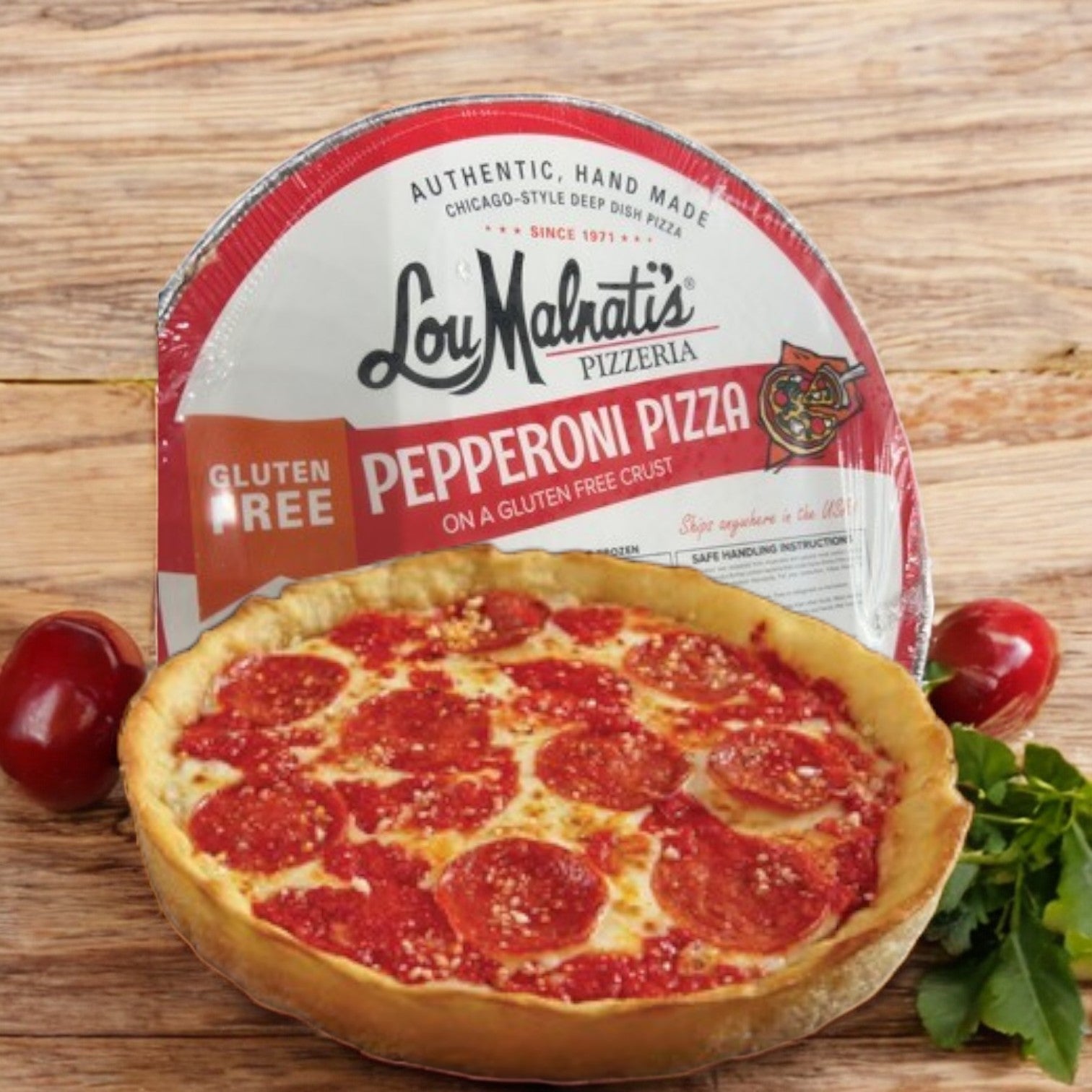 A 27.5 oz. Gluten Free Pepperoni Pizza Deep Dish from Lou Malnati's is beautifully displayed in front of its package on a wooden surface, accented by vibrant red tomatoes and fresh leafy greens.
