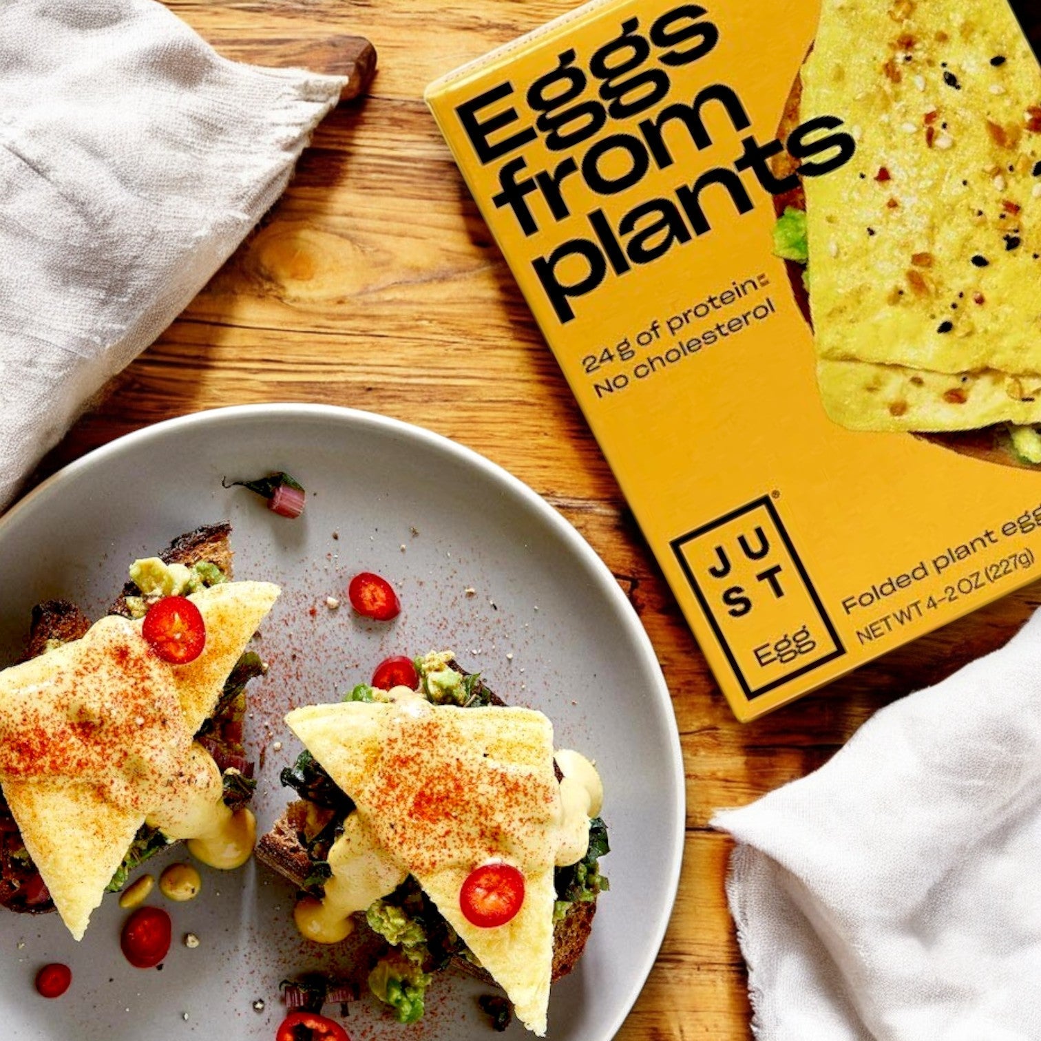 Two plates with plant-based Just Egg Folded on toast, garnished with sliced red chilies, highlight the cholesterol-free appeal of this dish. A box labeled "Just Egg Folded," touting mung bean protein as a key ingredient, sits nearby.