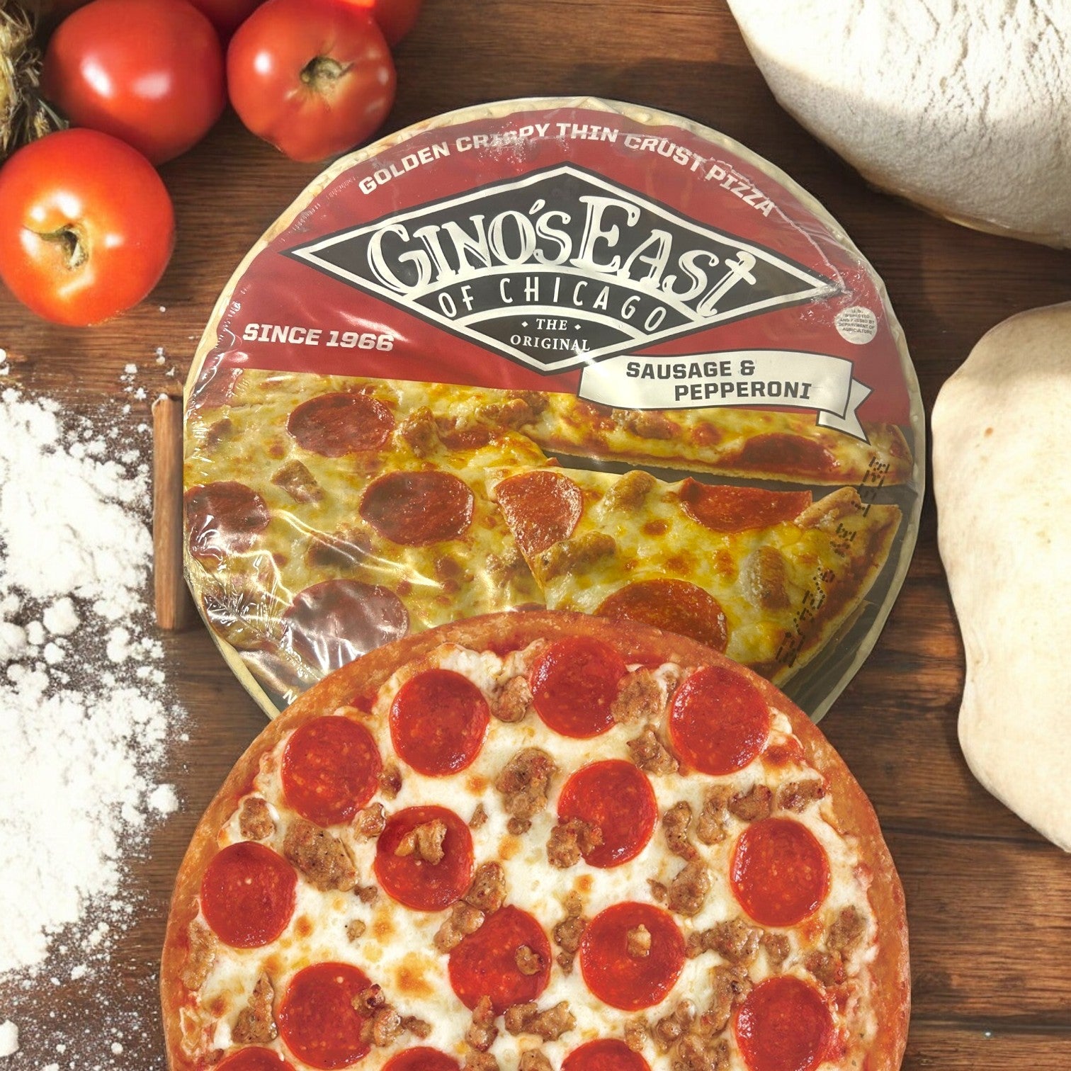 Gino's East Pizza presents their 14.7 oz Sausage & Pepperoni Pizza, a tribute to classic Chicago tavern-style pies, displayed with its packaging on a rustic wooden surface adorned with dough, tomatoes, and flour.