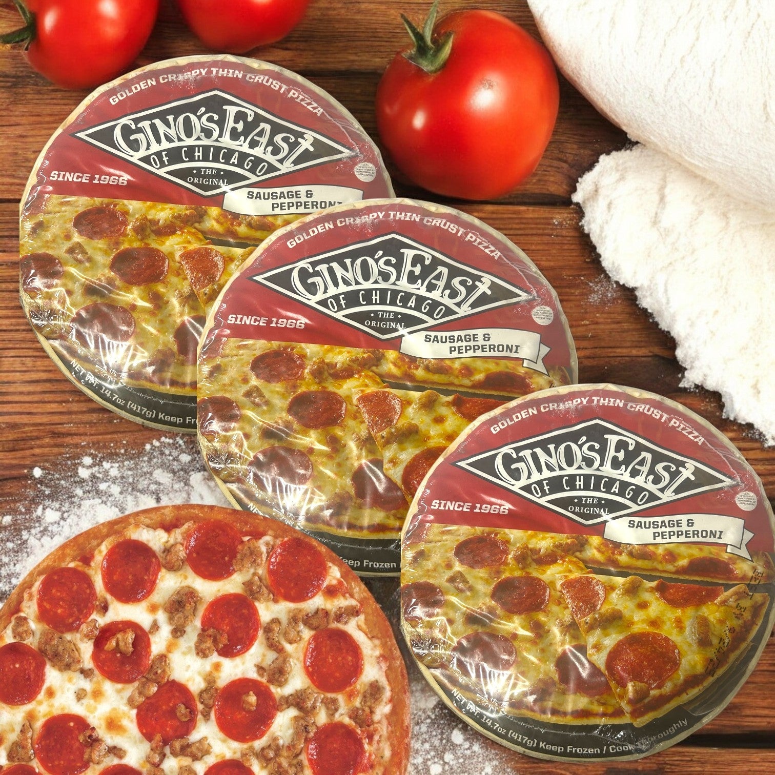 Three Gino's East of Chicago Sausage & Pepperoni Deep Dish Pizzas (14.7 oz each, total 50.1 oz) sit on a wooden surface, surrounded by tomatoes, flour, and a freshly baked thin crust pizza.