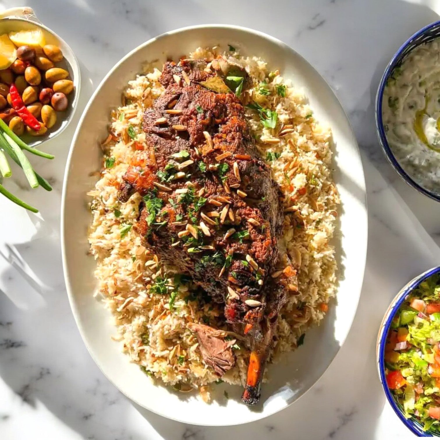 Tender and juicy Kirkland Signature Halal Boneless Leg of Lamb crowns seasoned rice, garnished with nuts and herbs. This delightful dish is encircled by small bowls of mixed vegetables, olives, and chili peppers on a pristine white surface.