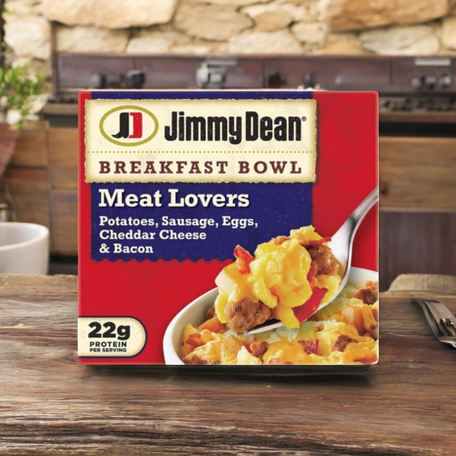 On a wooden counter sits a box of Jimmy Dean Breakfast Bowl, Meat Lovers, 8 Count - 3 Pack. It features potatoes, savory sausage and bacon, eggs, and cheddar cheese. With 22g protein per serving, it's an ideal protein-rich breakfast option.