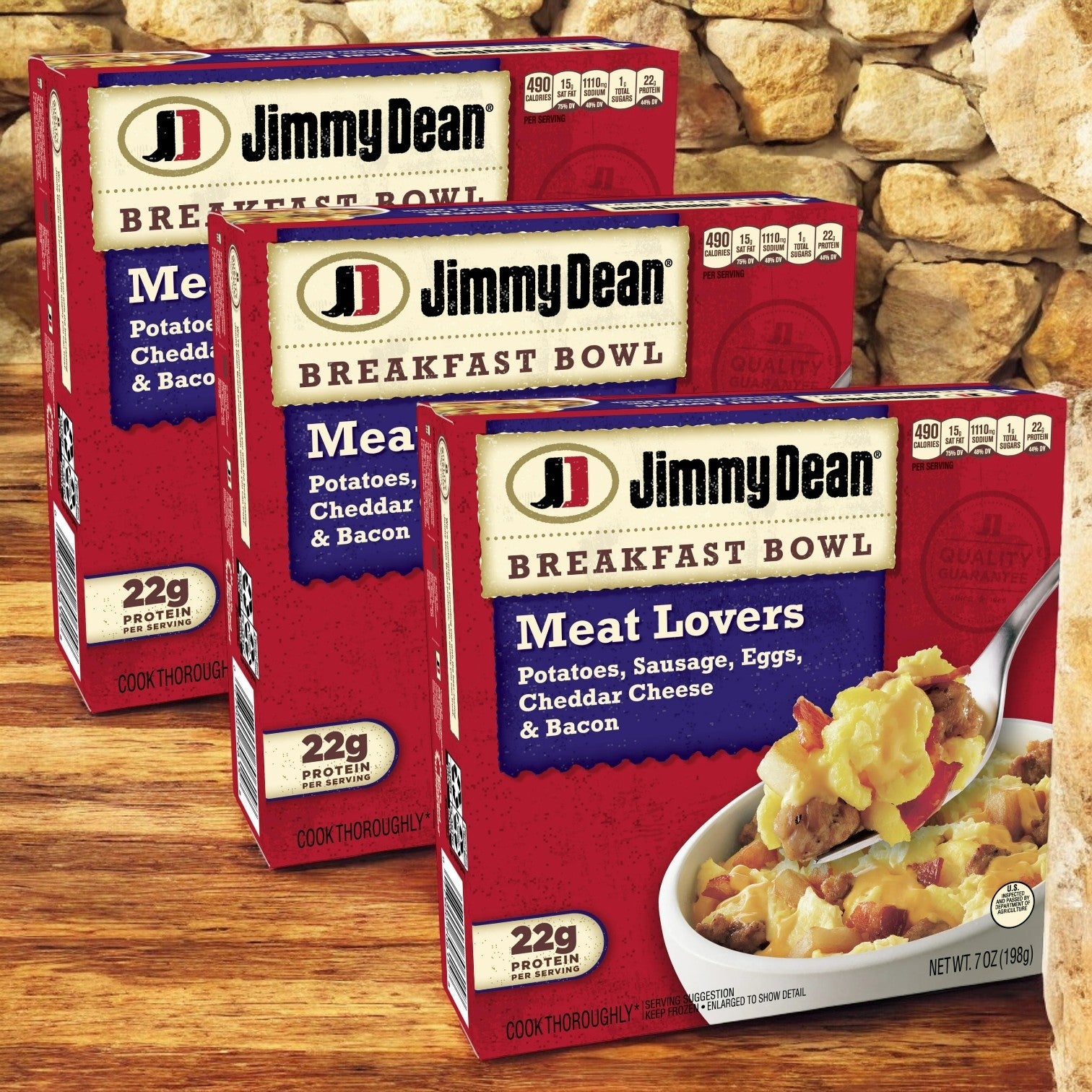 Three packs of Jimmy Dean Breakfast Bowl, Meat Lovers (8 count each), known for their protein-rich blend with potatoes, sausage, eggs, cheddar cheese, and bacon, are placed in front of a stone wall.
