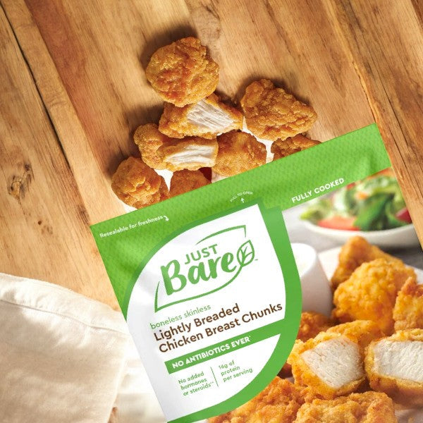A package of Just Bare Lightly Breaded Chicken Breast Chunks, Boneless Skinless, 4lbs - 1 Pack is displayed on a wooden surface, with some delicious chicken pieces spilling out of the bag.