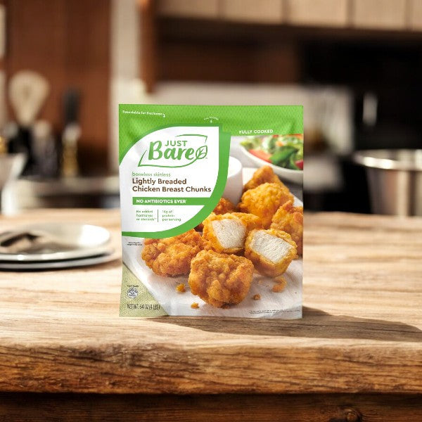 A 4-pound pack of Just Bare Lightly Breaded Boneless Skinless Chicken Breast Chunks is placed on a wooden kitchen counter, with a blurred kitchen scene in the background, showcasing the premium quality from Just Bare.