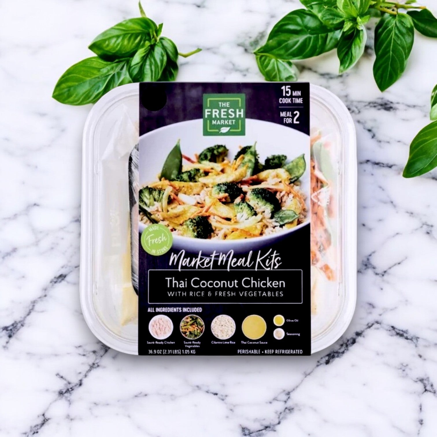 The Fresh Market Thai Coconut Chicken with Rice & Fresh Vegetables Market Meal Kit (36 oz) rests on a marble surface, showcasing rice and vibrant vegetables, enhanced by fresh basil leaves for authentic Thai flavors.