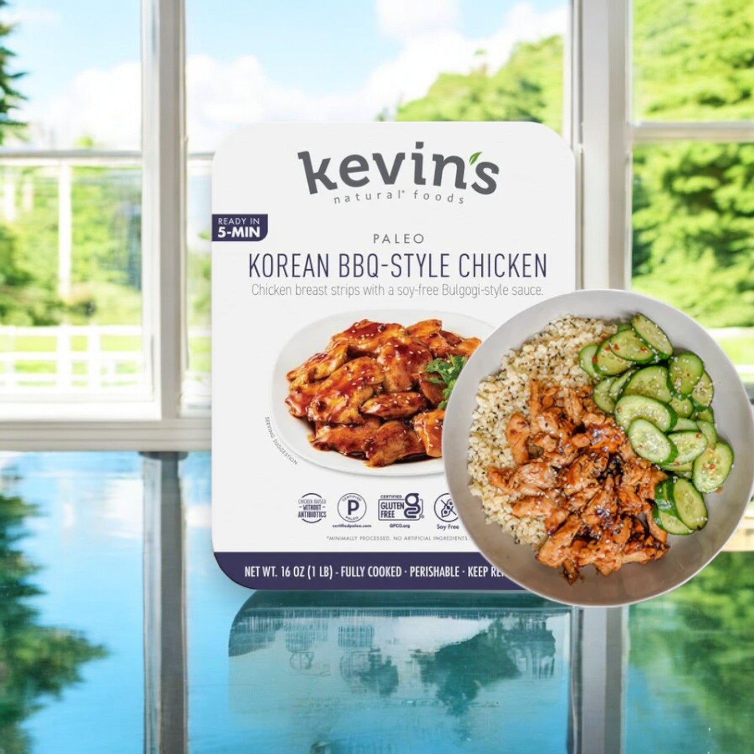 A pack of Kevin's Korean BBQ-Style Beef sits next to a plate filled with authentic flavors: juicy beef, cauliflower rice, and sliced cucumbers, all set against the backdrop of a bright window for a perfect Korean BBQ feast.