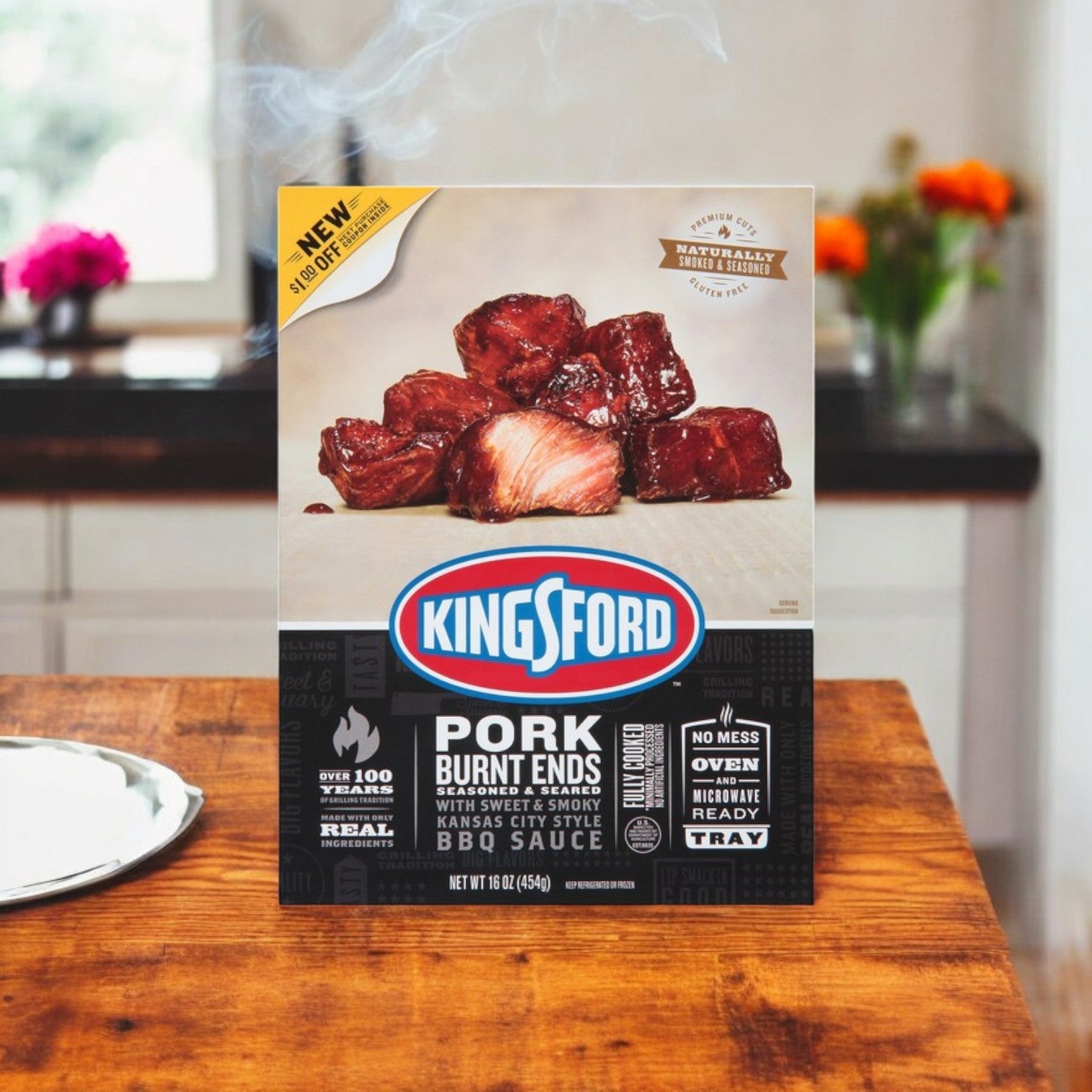 A box of Kingsford BBQ Feast – Pulled Pork, Baby Back Ribs & Burnt Ends sits on the kitchen counter, featuring sauced meat pieces ready for the oven. The packaging emphasizes their convenience and rich barbecue flavor while pulled pork subtly enhances the inviting backdrop.