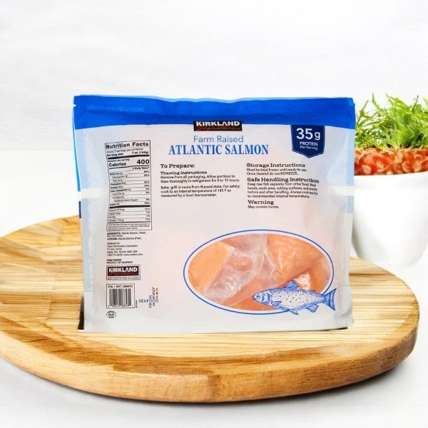 A wooden board holds a bag of Kirkland Signature Atlantic Salmon, 6 oz - 8 oz center-cut portion. Paired with a herb bowl, it's sustainably farm-raised, includes nutrition facts and storage instructions, and is rich in omega-3s for a healthy option.