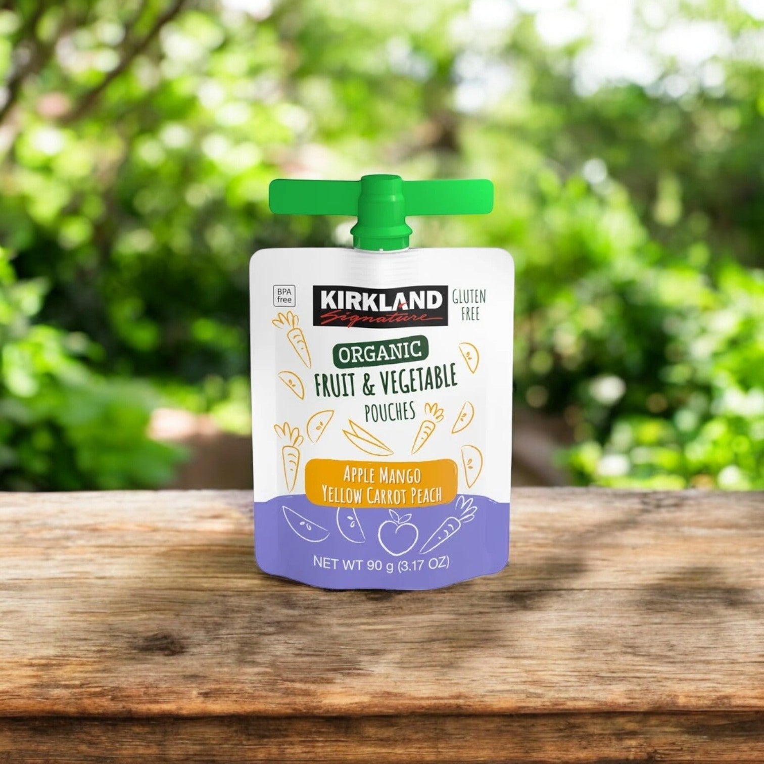On a wooden surface, a pouch with a green cap reads "Kirkland Signature Organic Fruit and Vegetable Pouches Variety Pack." Embrace health with this 24-count, 3.17 oz pack of apple mango yellow carrot peach flavor set against gentle greenery.
