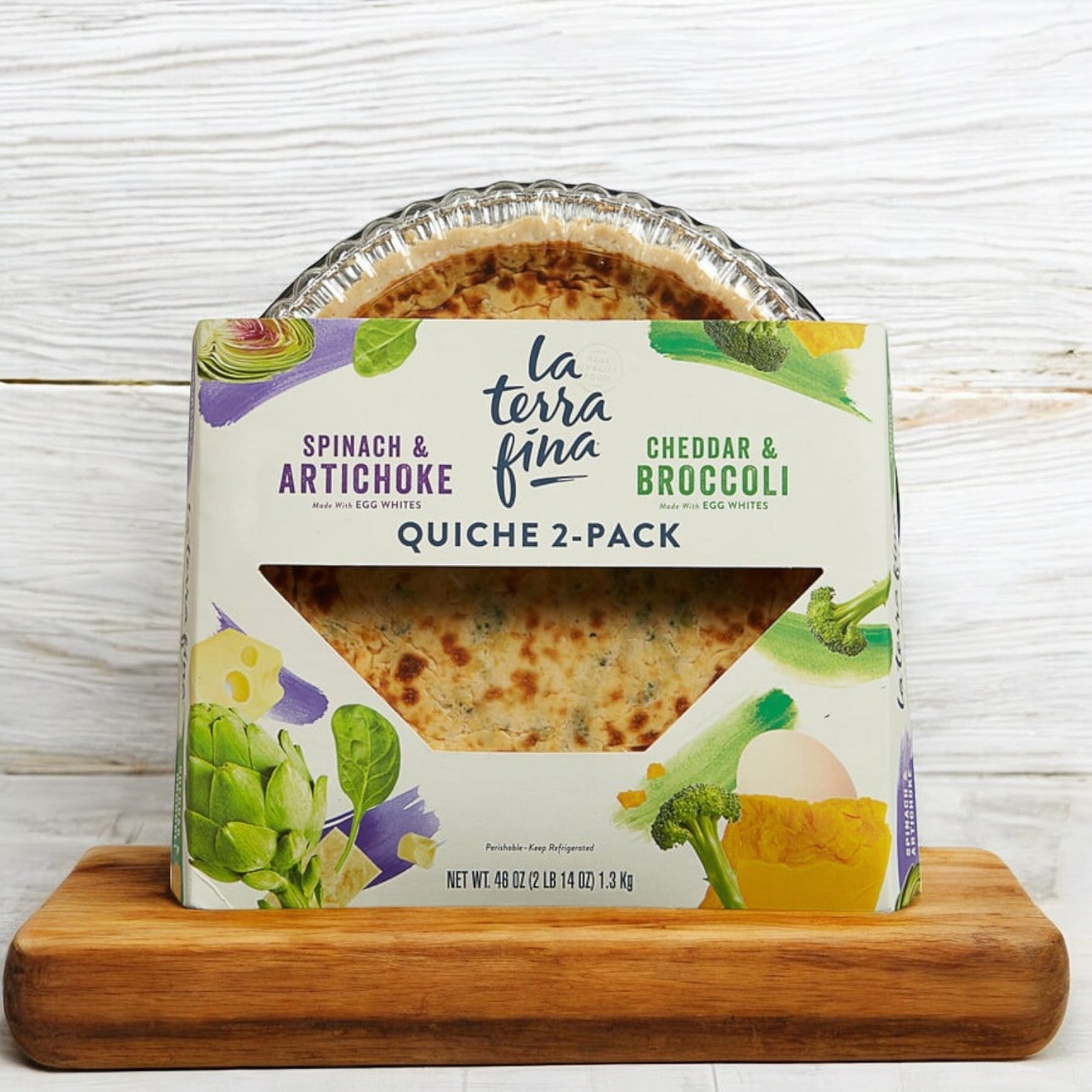 A La Terra Fina Quiche 2-Pack, 46 oz., featuring spinach, artichoke, cheddar, and broccoli varieties is elegantly displayed on a wooden board, offering a delectable gourmet frozen meal.