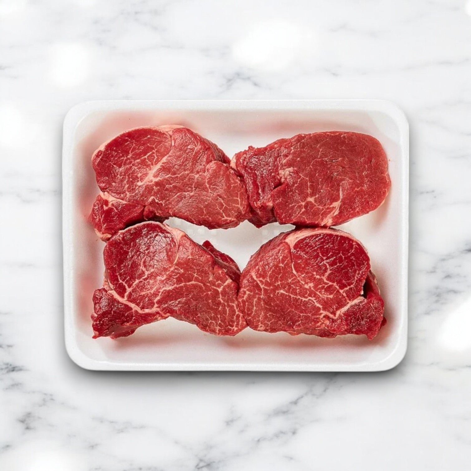 Four USDA Choice Beef Loin Tenderloin Steaks sit in a white foam tray, their marbling reflecting the elegance of the marble below, paired perfectly with Easy Lunches' Surf and Turf offering: Filet Mignon & 5 pounds of frozen Netuno Lobster Tails.