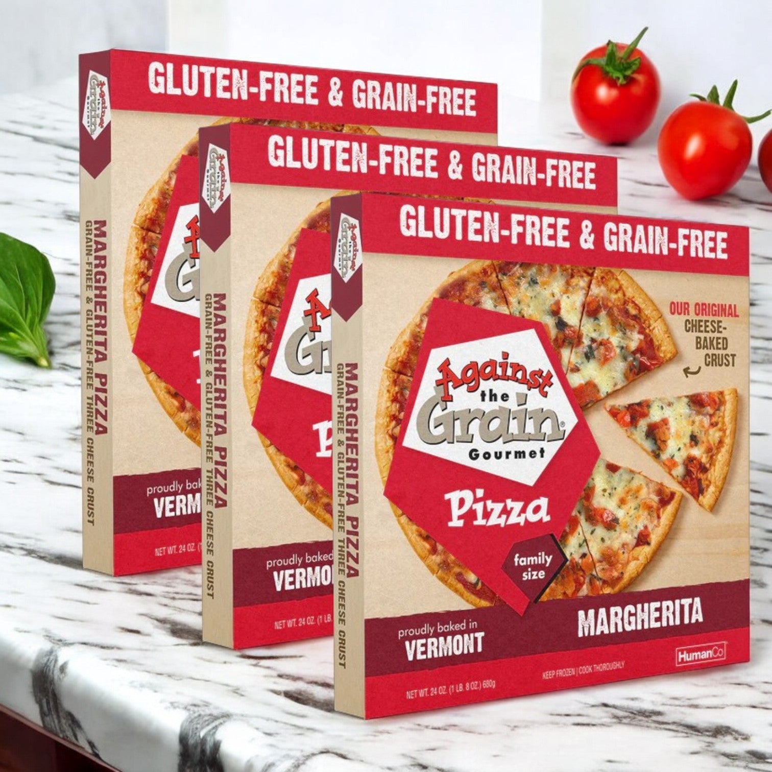 On a marble counter, three boxes of Against the Grain Gourmet Pizza, Margherita Pizza, Gluten-Free - 72 oz., are displayed alongside vibrant cherry tomatoes.