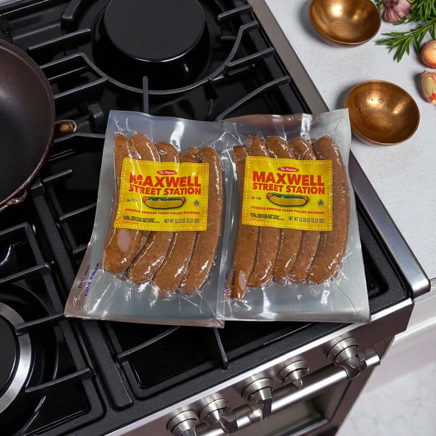 A pack of Vienna Beef Maxwell Street Station Famous Smoked Fresh Polish Sausage, 53.33 oz., is placed on a stove next to a frying pan and kitchen utensils.