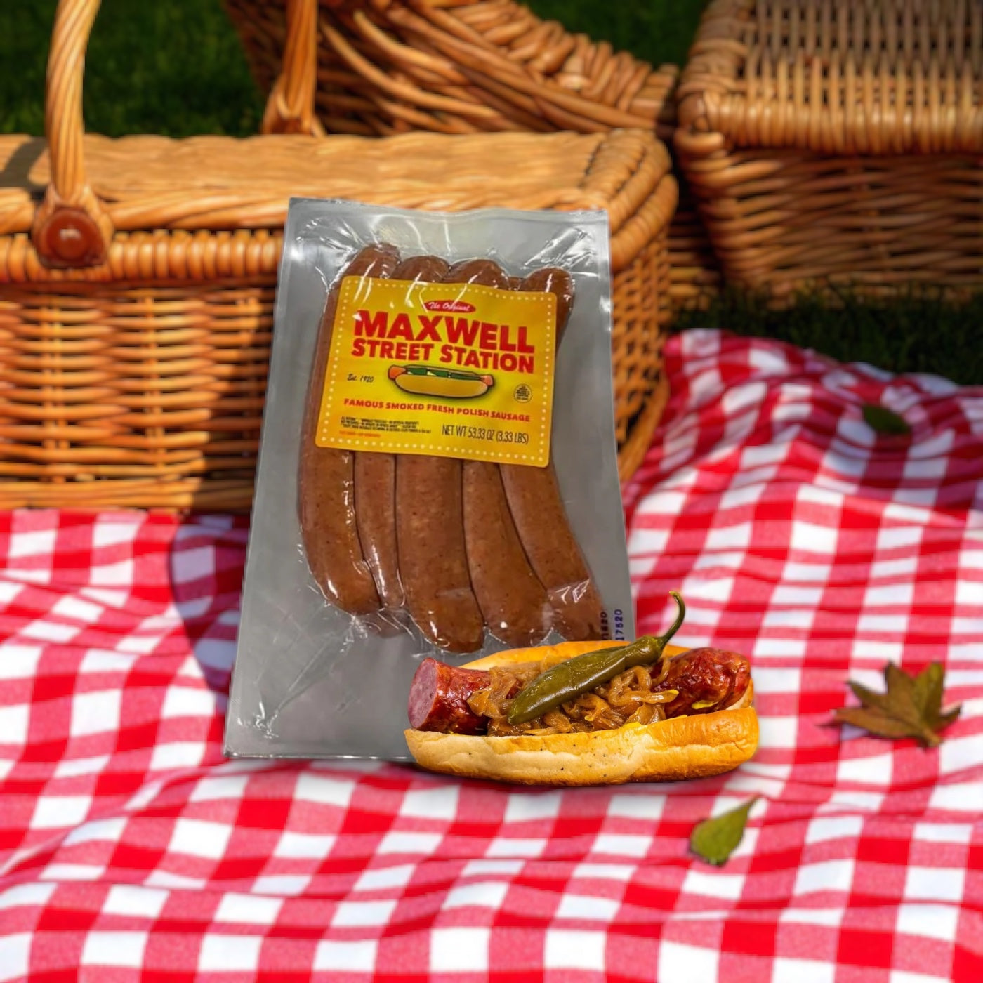 A pack of Vienna Beef Maxwell Street Station Famous Smoked Fresh Polish Sausage, 53.33 oz., rests on a red and white checkered picnic blanket beside a topped bun with picnic baskets in the background.