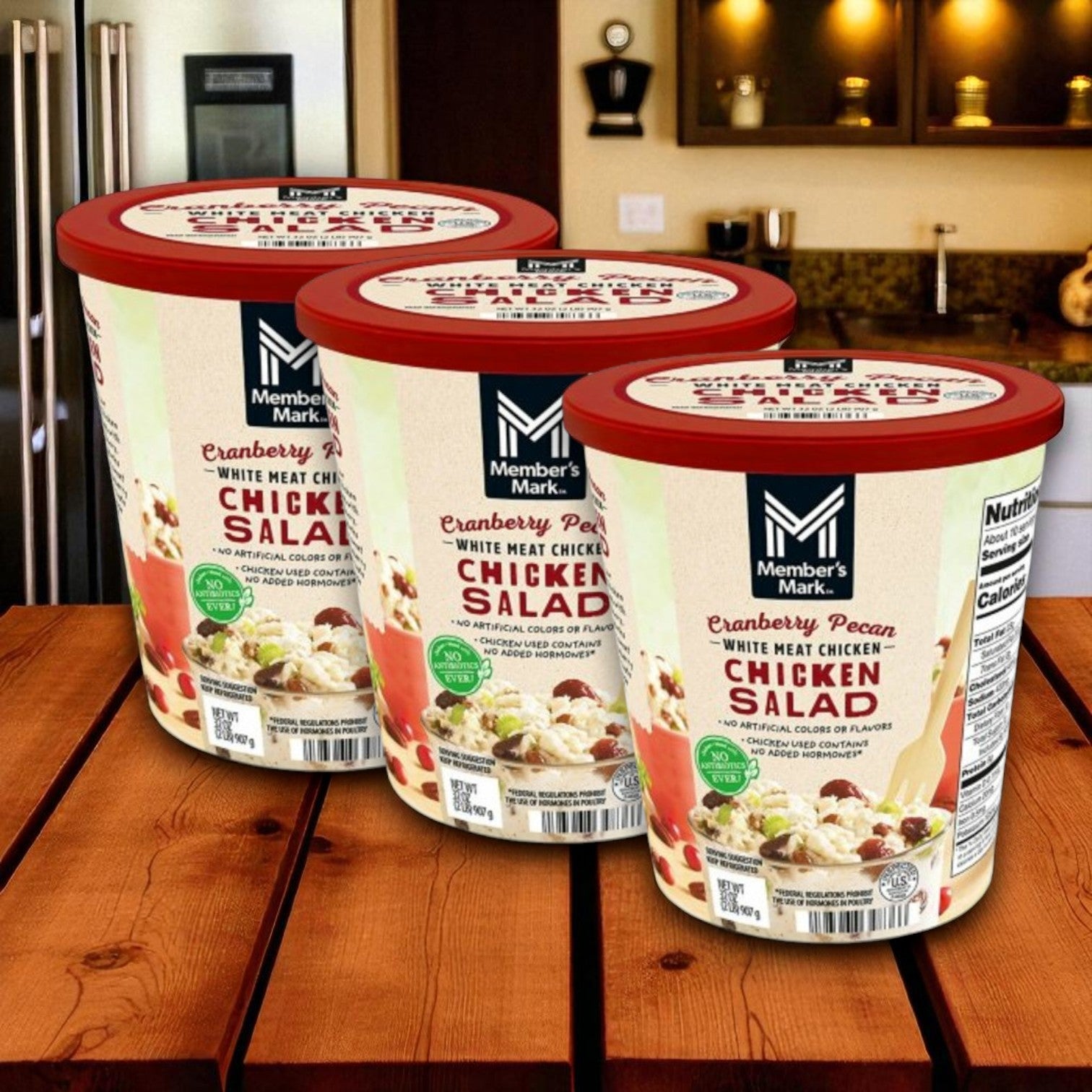 Three 2-lb cases of Member's Mark Cranberry Pecan Chicken Salad are displayed on a wooden surface in a modern kitchen.