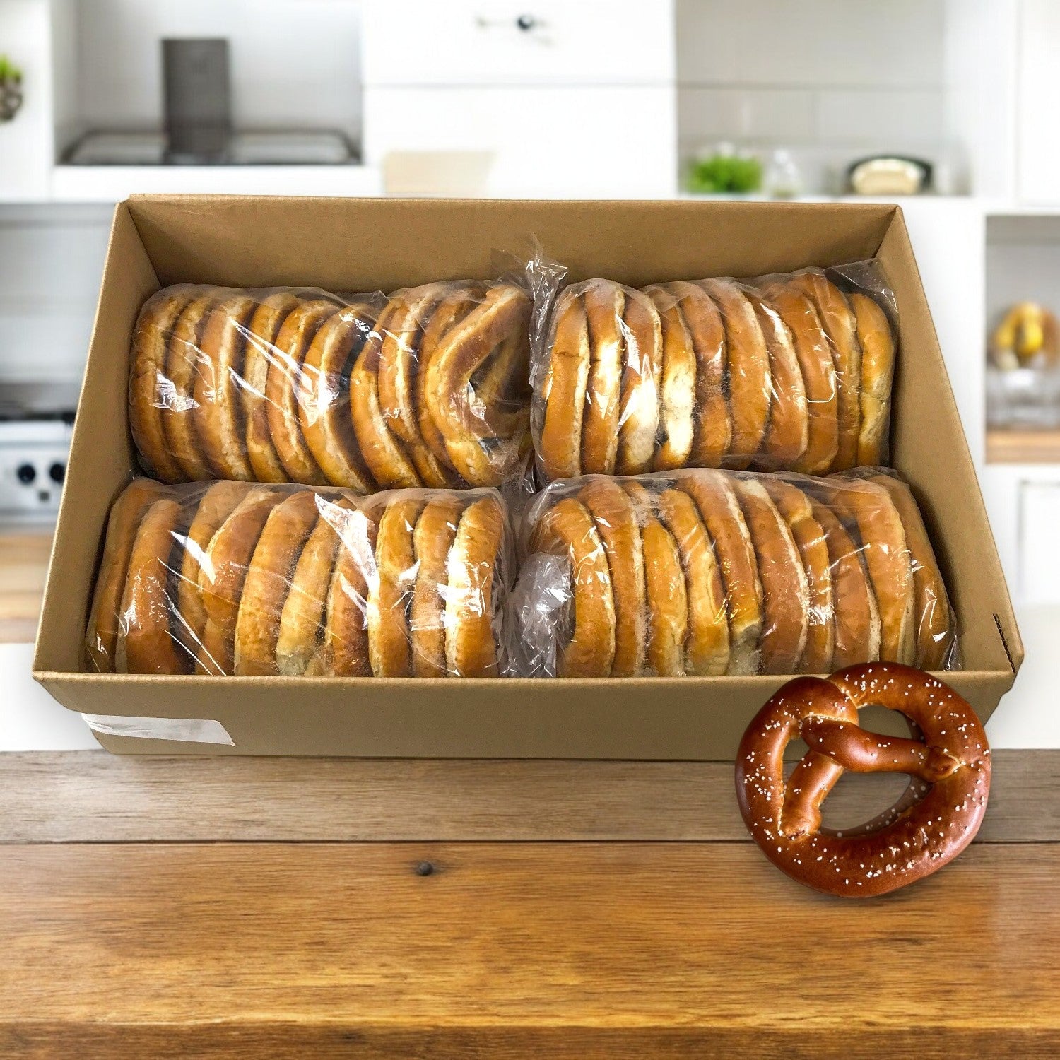 A cozy kitchen scene features a large box of bagels wrapped in plastic on a wooden surface, with a salted Bavarian pretzel from Milwaukee Pretzel Company nearby, hinting at the authentic flavor of Super Pretzel’s Bavarian Twist Pretzels (4 packs of 10, 5 oz each).