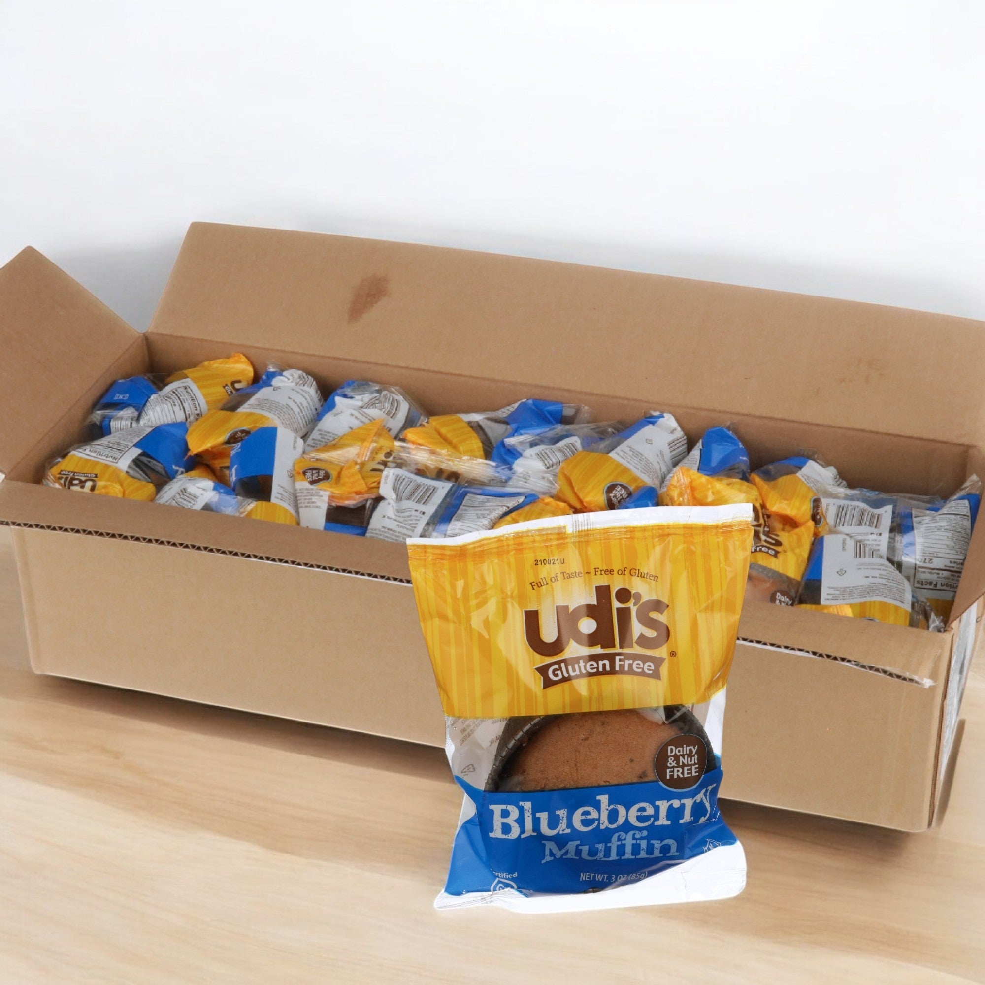 A cardboard box filled with Udi's Gluten Free Blueberry Muffins, each a 3 oz. individually wrapped treat bursting with fresh blueberries. One package sits upfront, promising to delight your taste buds. Available as a case of 36 count.