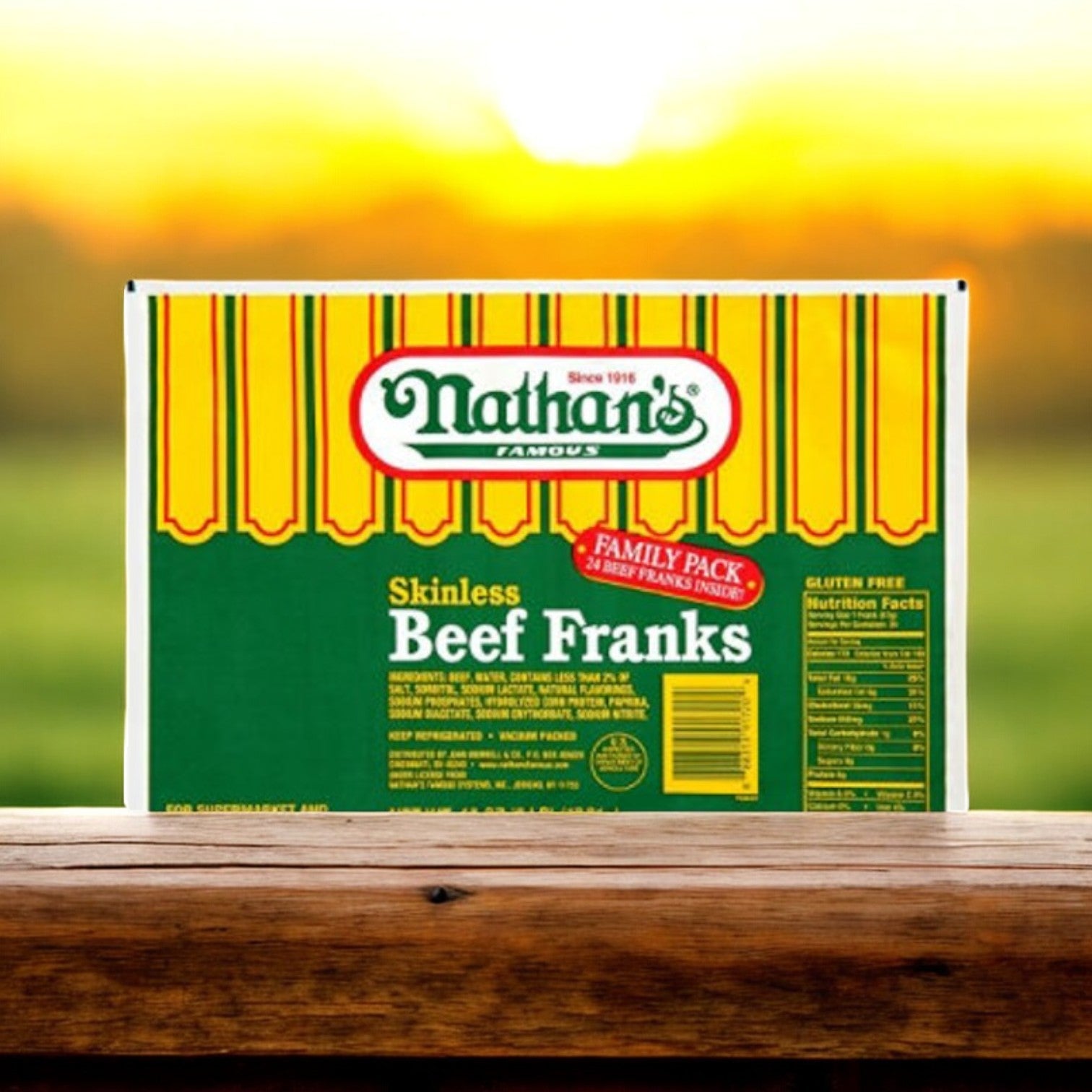 A pack of Nathan's Famous Skinless Beef Franks, featuring the 3.2 oz each, 5 lb pack of 24 franks, is set against a sunrise backdrop with its vibrant yellow and green packaging highlighting the nutritional information on the side.
