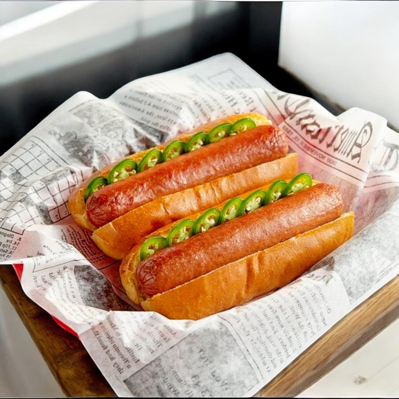 Two Nathan's Famous Colossal Quarter Pound Beef Franks in buns topped with sliced jalapeños sit on a newspaper-lined tray.