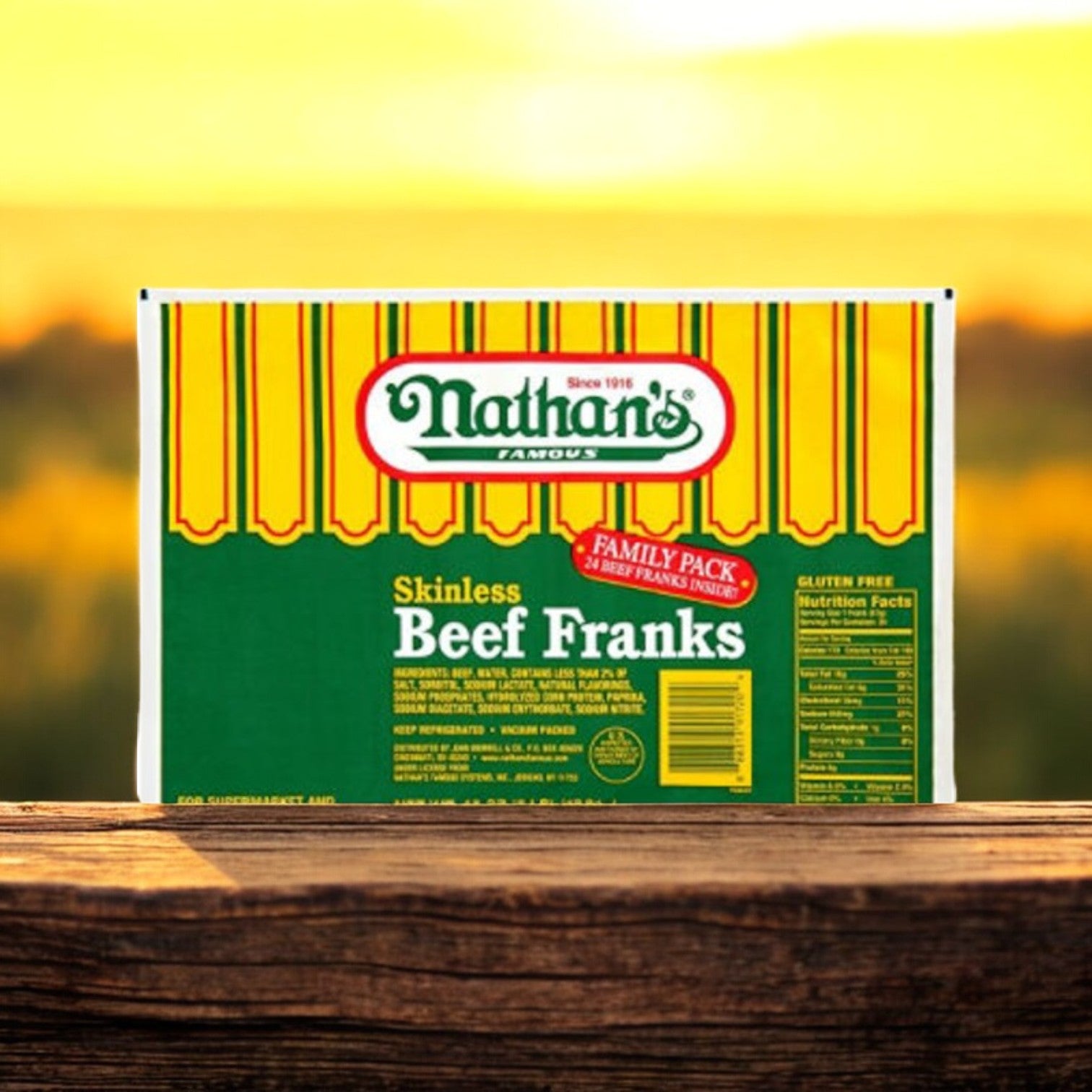 A box of Nathan’s Famous Skinless Beef Franks, 2 oz each in a 5 lb pack with 24 franks, features a yellow and green design labeled "Family Pack" on a wooden surface against a blurred natural background.