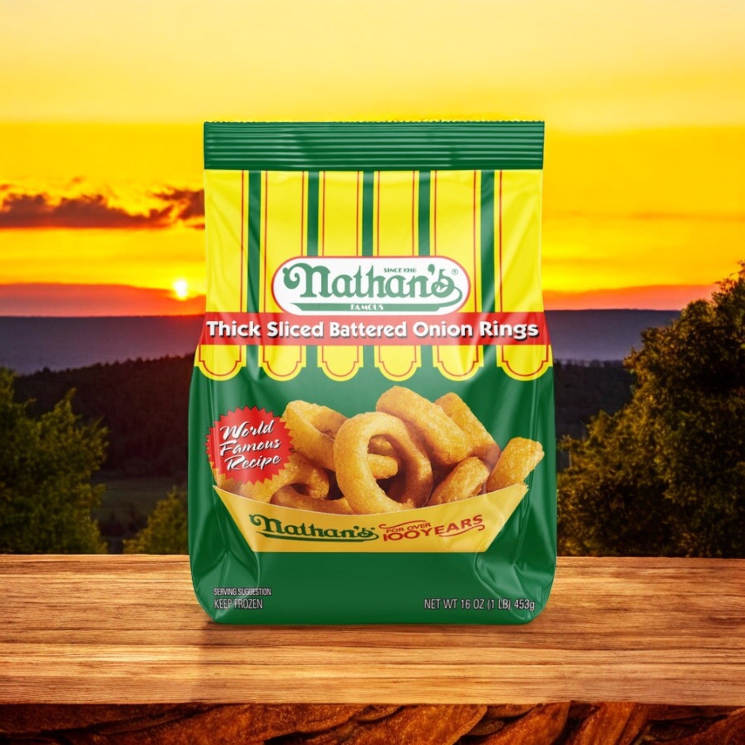 A package of Nathan's Famous Onion Rings, Battered, Thick Sliced – 16 oz - 3 Count rests on a wooden surface, with a scenic sunset backdrop featuring trees and hills.
