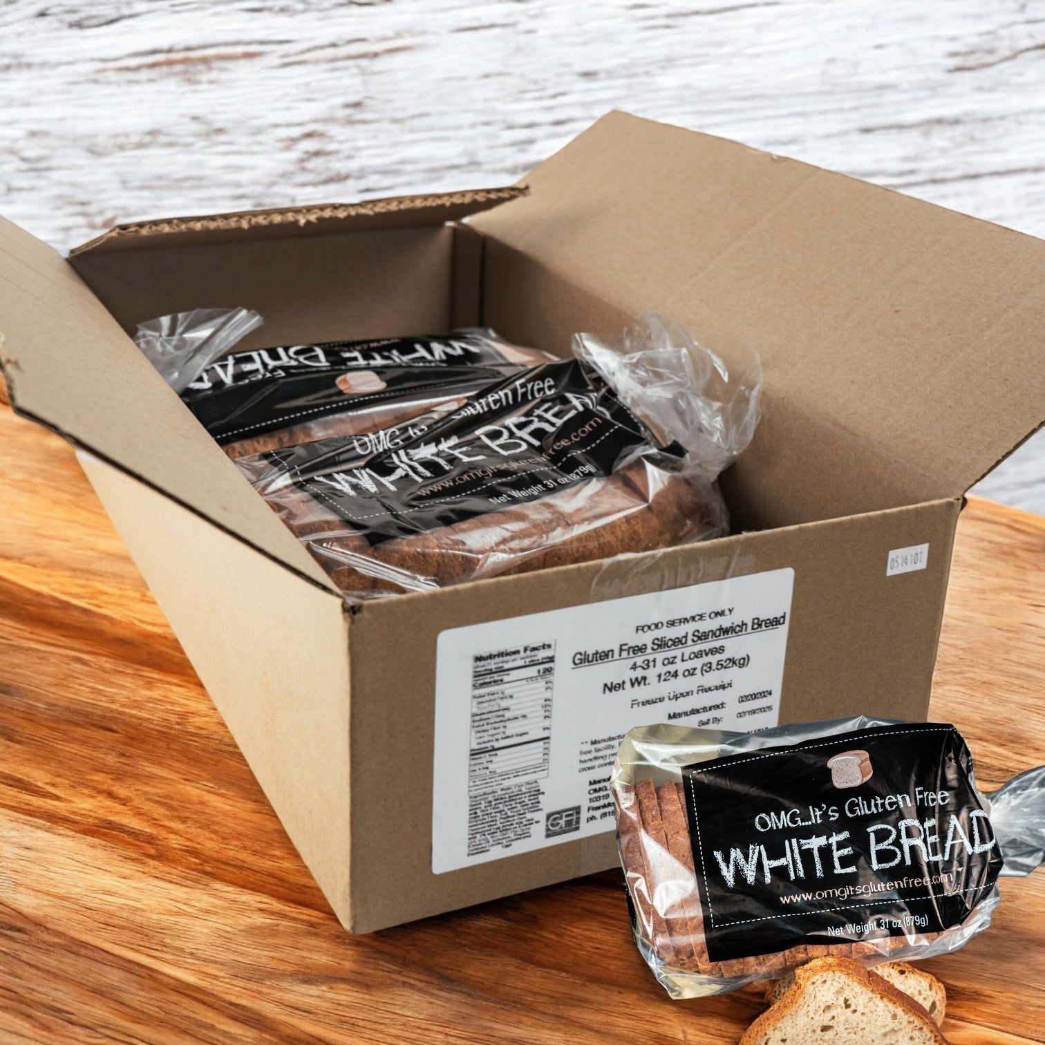 A wooden surface displays a loaf of OMG It's Gluten Free White Bread, 31 oz., taken out from a cardboard box containing multiple loaves, all made with premium ingredients from the 24-pack case.