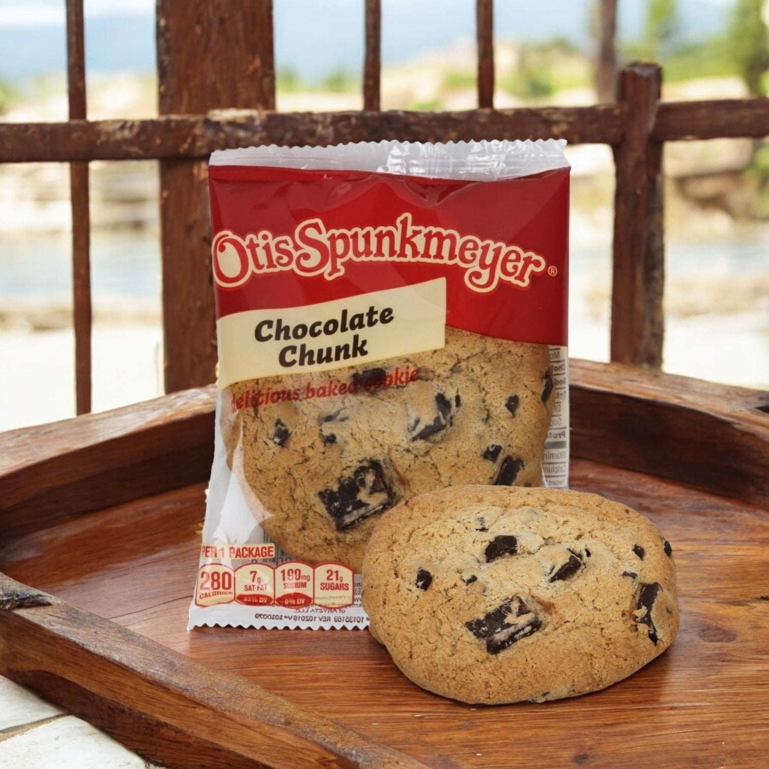 A delightful package of Otis Spunkmeyer Chocolate Chunk 2 oz. Cookies, 72 Count, sits on a wooden tray with one perfectly baked cookie displayed beside it.