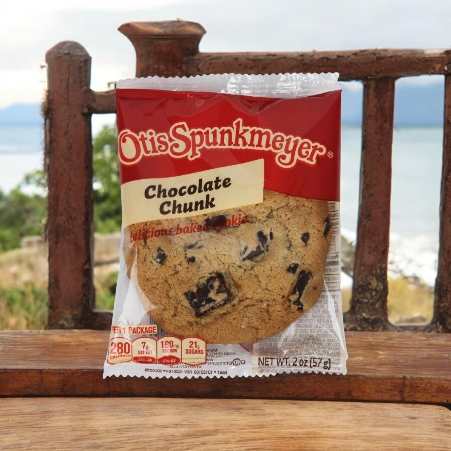 An individually wrapped Otis Spunkmeyer Blueberry Muffin 2.25 oz. rests on a wooden bench, with a blurred outdoor landscape in the background.