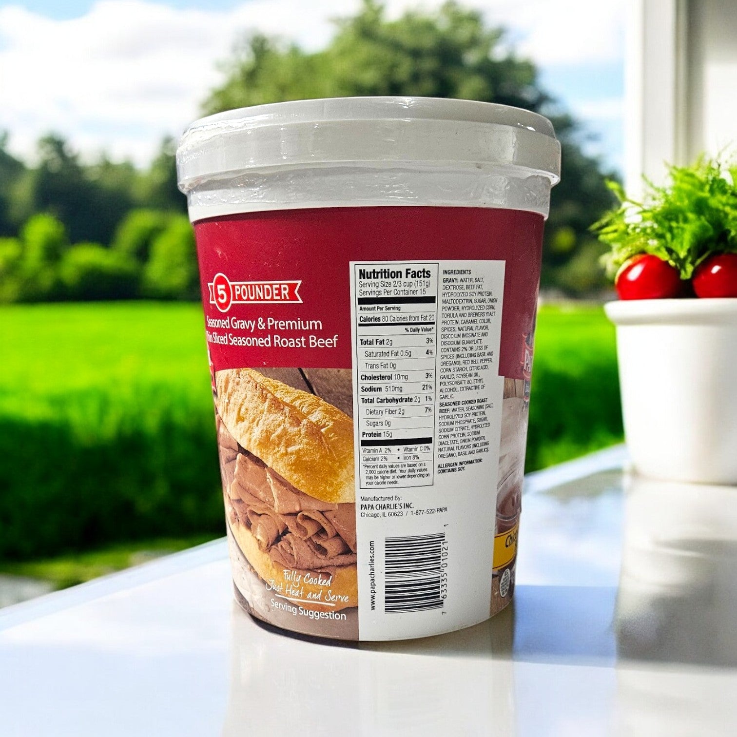 Three containers of Papa Charlie's Thin Sliced Roast Beef, each 5 pounds, featuring seasoned gravy and nutritional info on the label, rest on a white surface near a window with a potted plant.