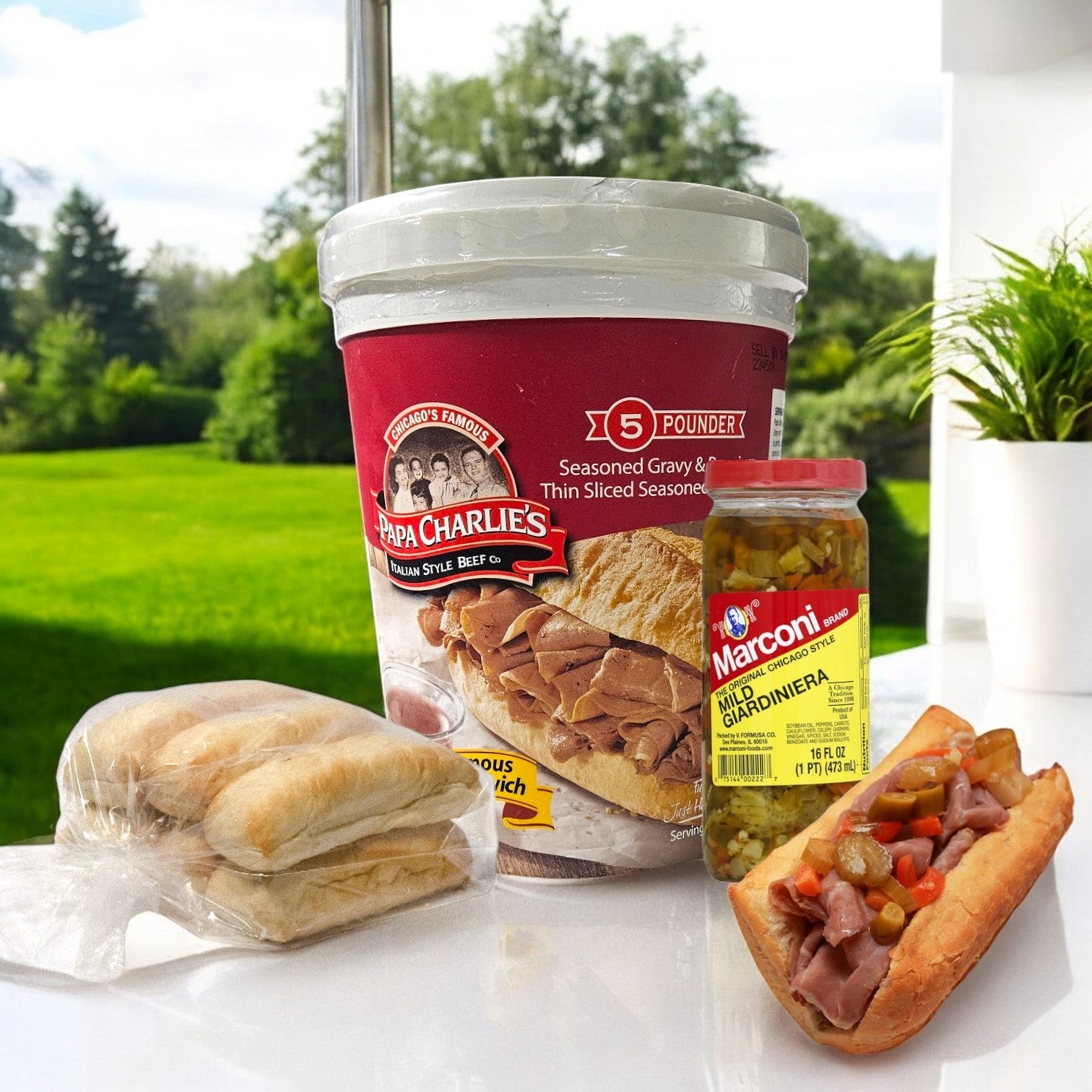 A Papa Charlie's 32 Sandwich Combo, which includes buns and mild giardiniera, is displayed outdoors on a table with a garden in the background.