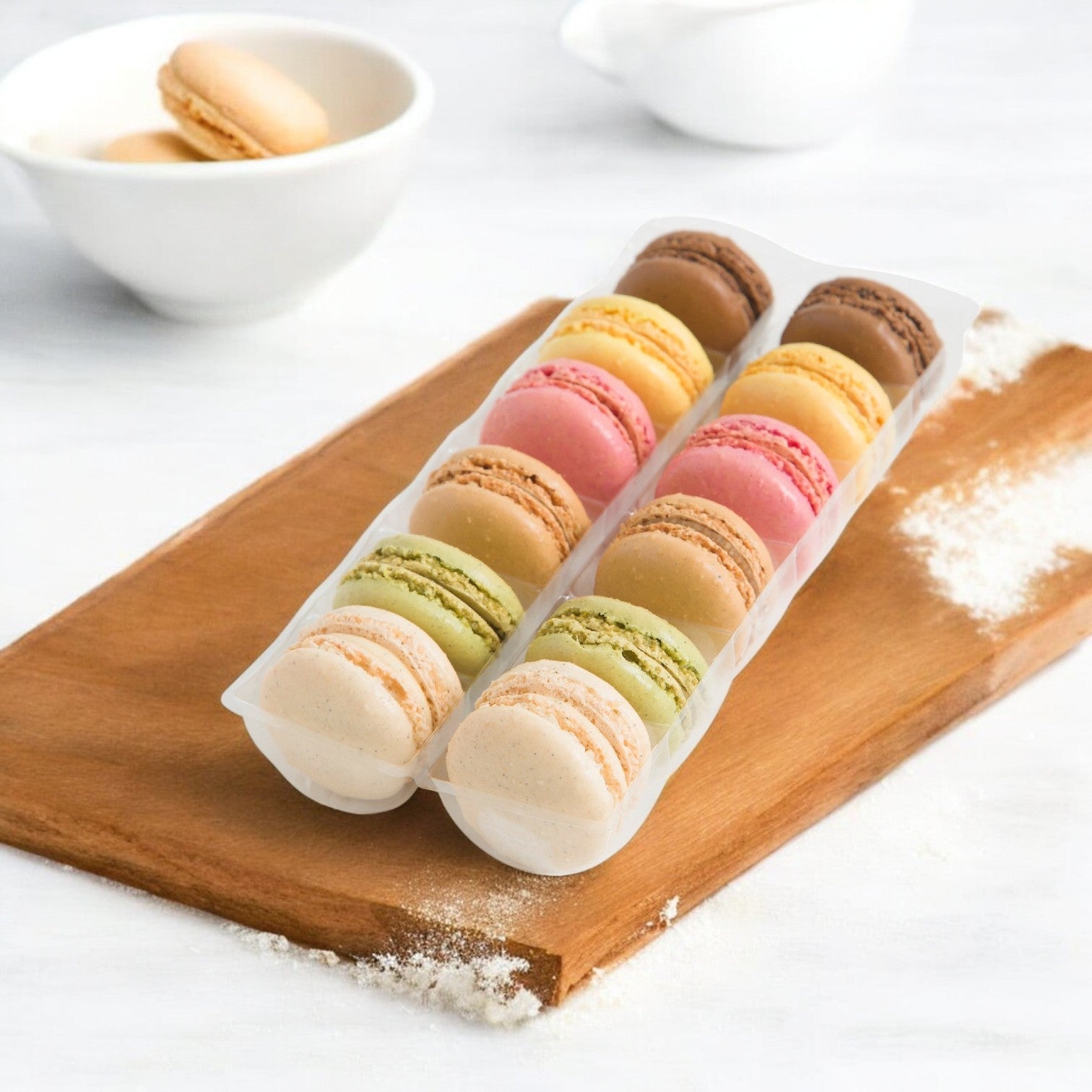 Pasquier Mini Assorted Macarons—2 trays of 72 each—exemplify French craftsmanship, displayed on a wooden board with flour against a white backdrop.