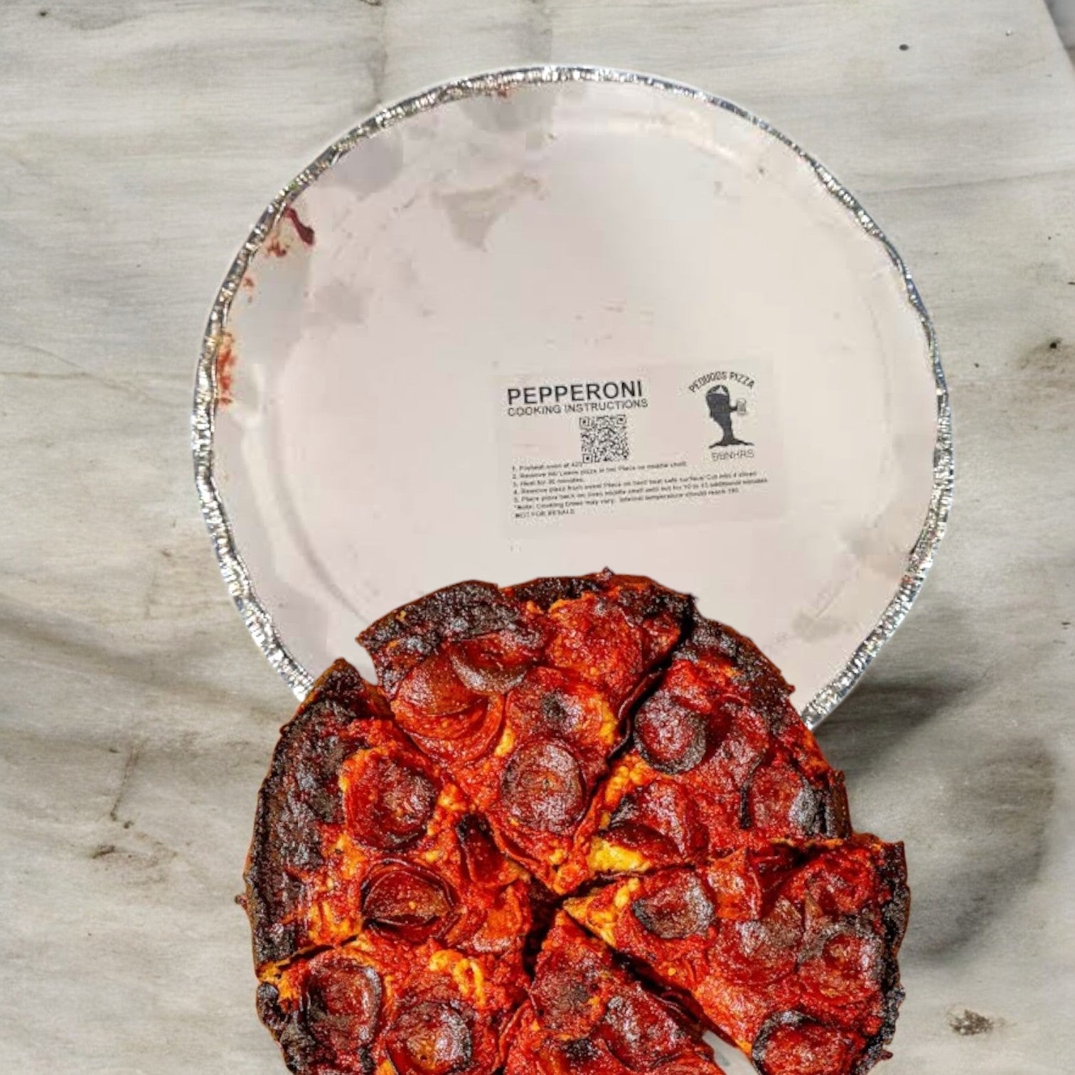 A burnt Pequod Pizza, Pepperoni 2" tall, sits on a foil pan with its label visible against the sleek marble surface—an unmistakable nod to the iconic style of Pequod's Pizza.