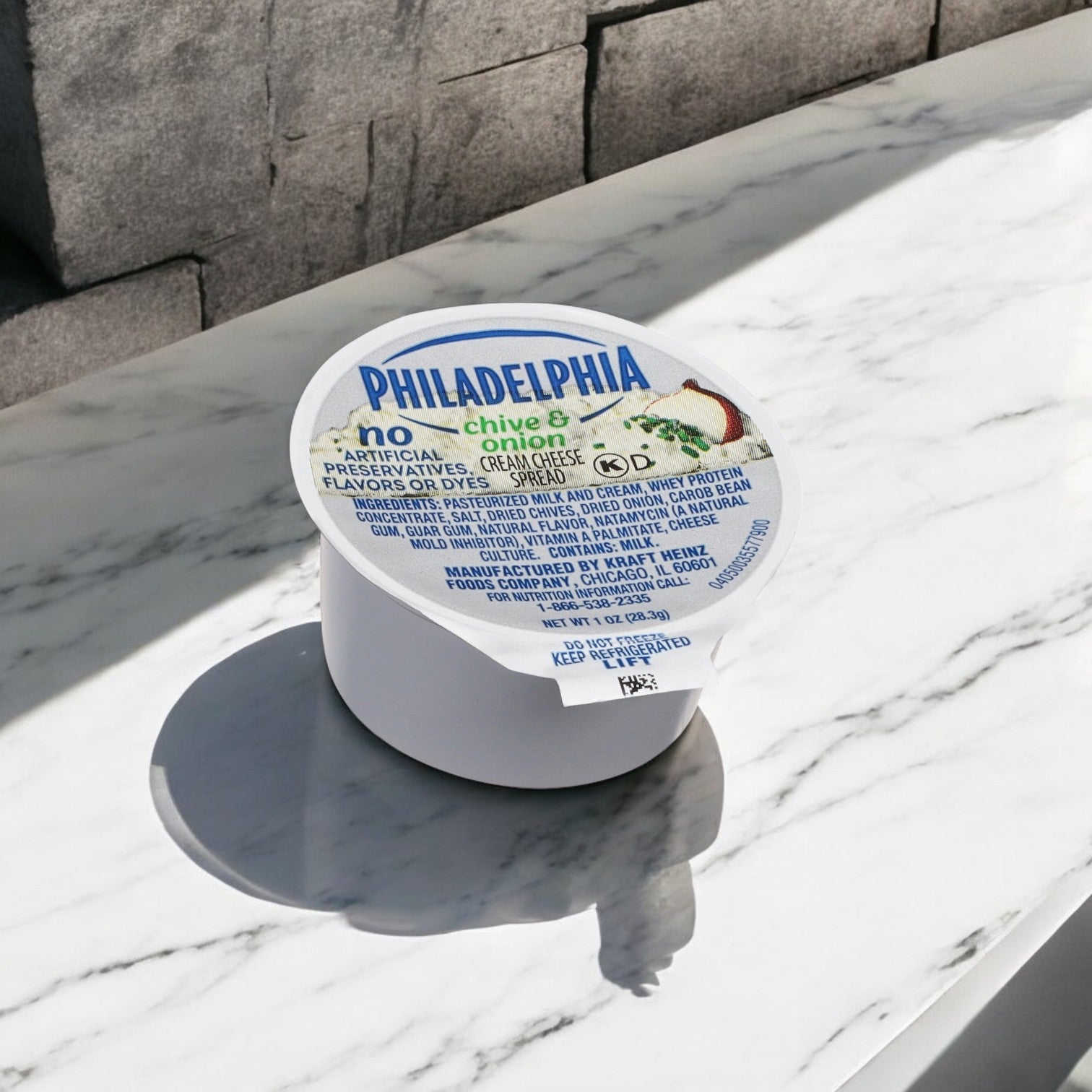 A Kraft Philadelphia Cream Cheese, Chive & Onion Spread Cup (1 oz.) sits on a sunlit marble surface, basking in the glow.